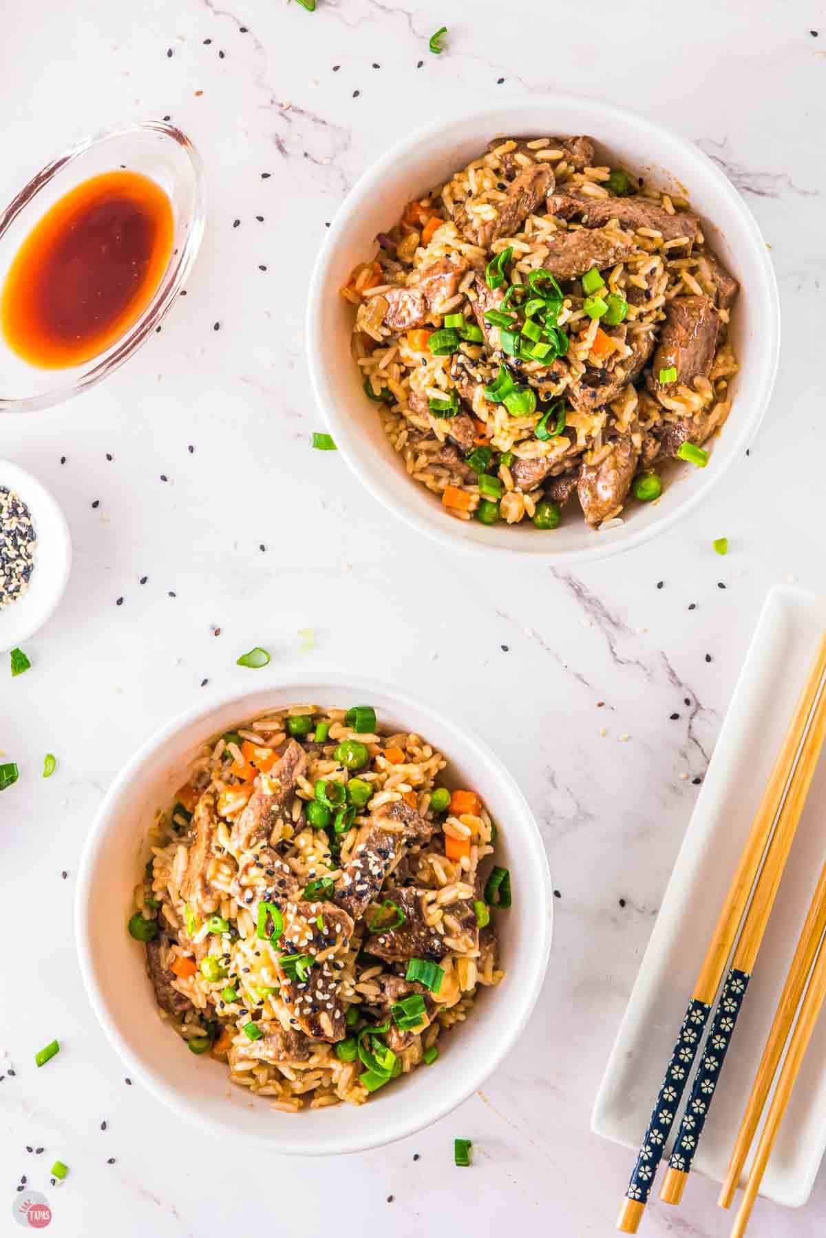 two bowls of steak fried rice next to a plate with chopsticks