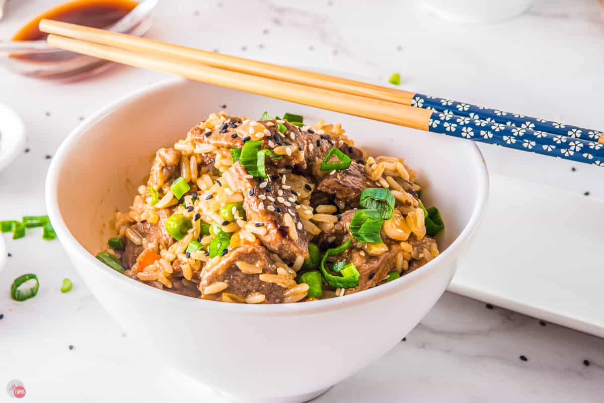 close up of steak fried rice in a white bowl with chopsticks on top