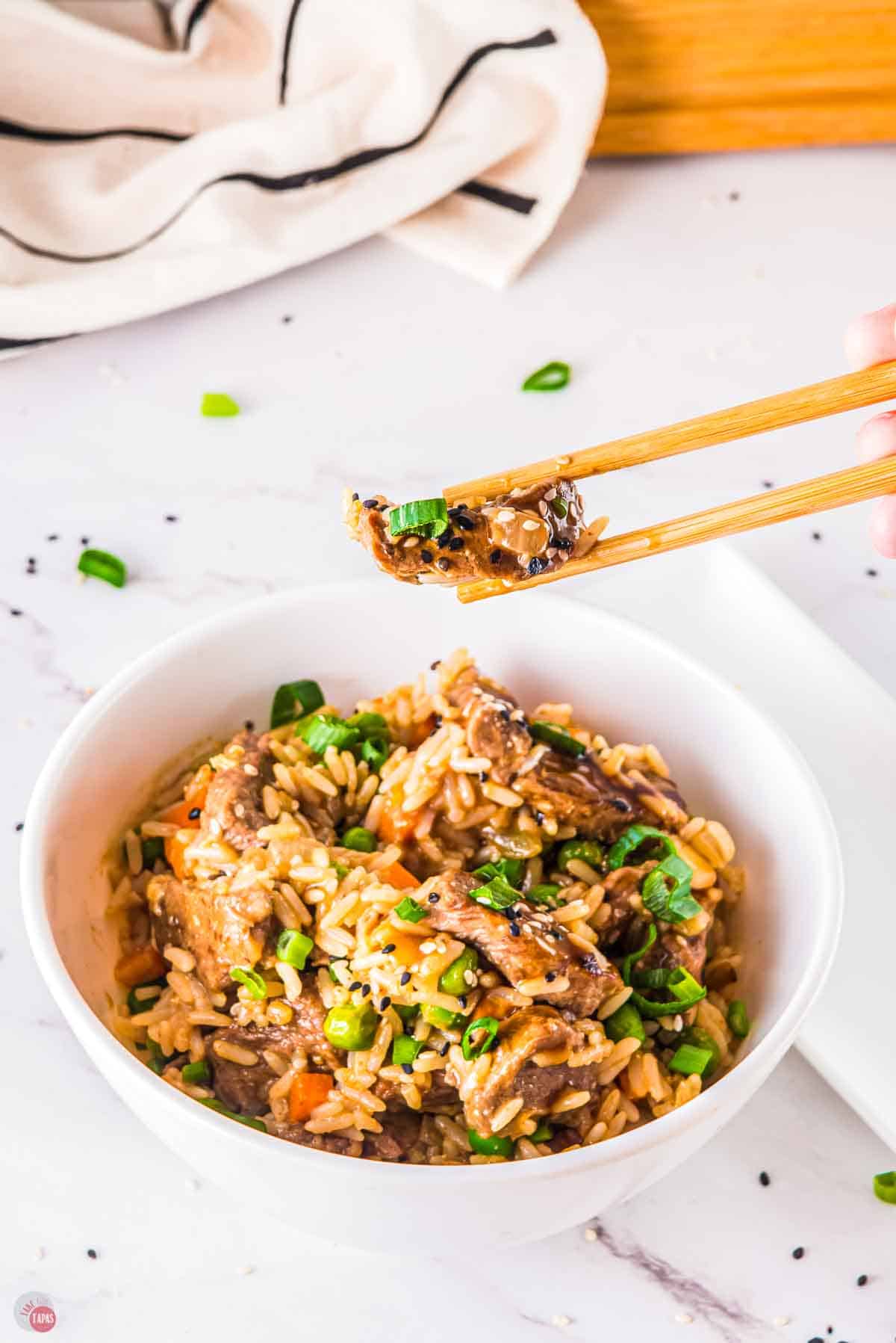 chopsticks with a bite of fried rice over a bowl