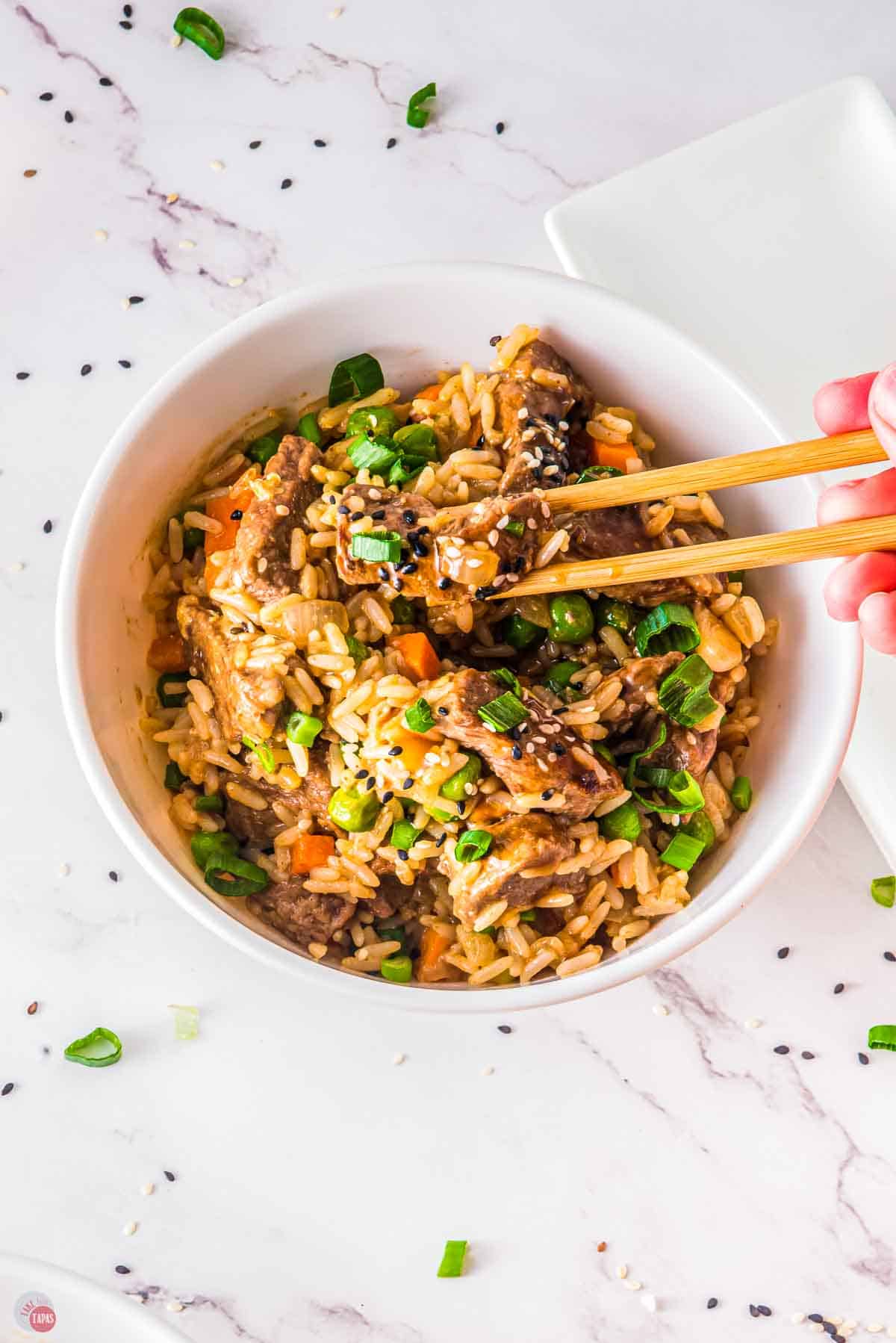 bowl of steak fried rice with chop sticks picking up a piece