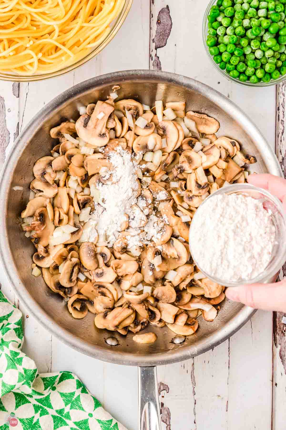 mushrooms and onions simmering in a skillet with flour being sprinkled on top