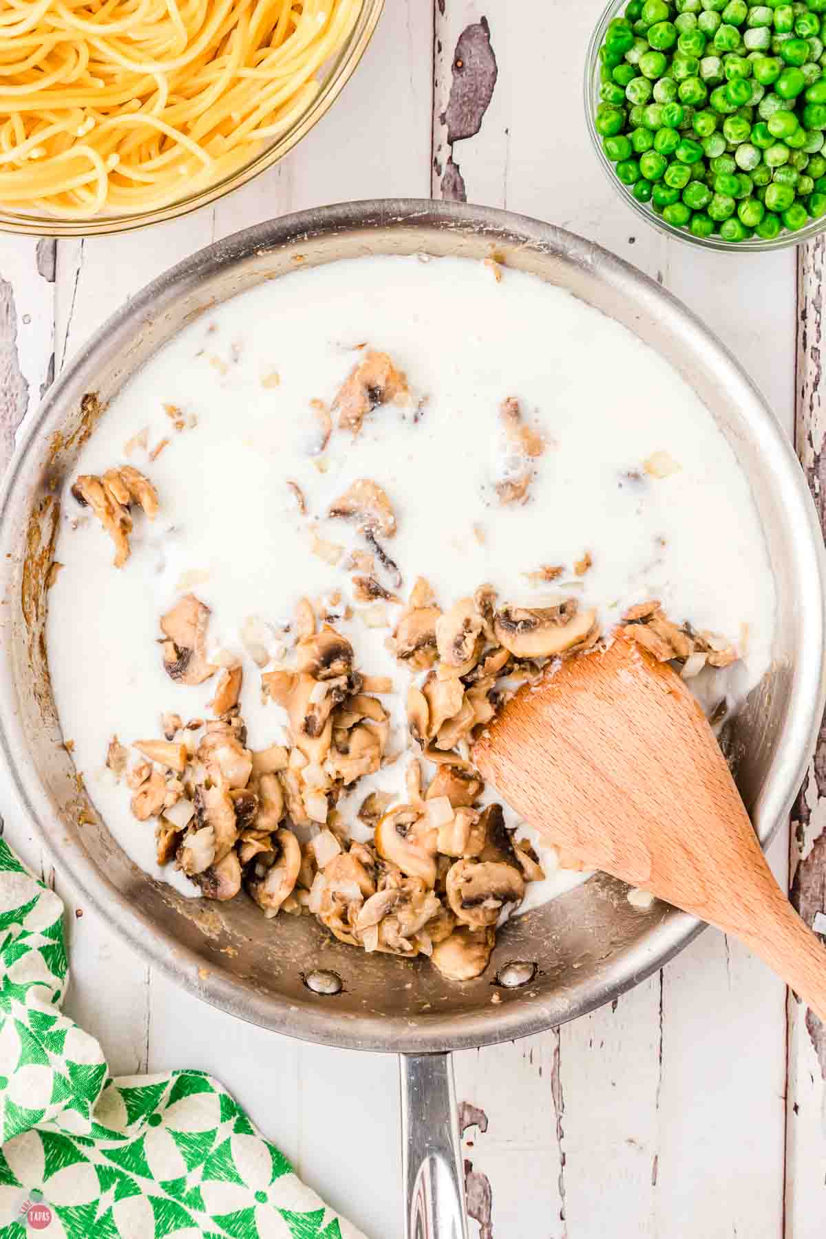 wood spoon stirring milk into sauteed mushrooms in a skillet