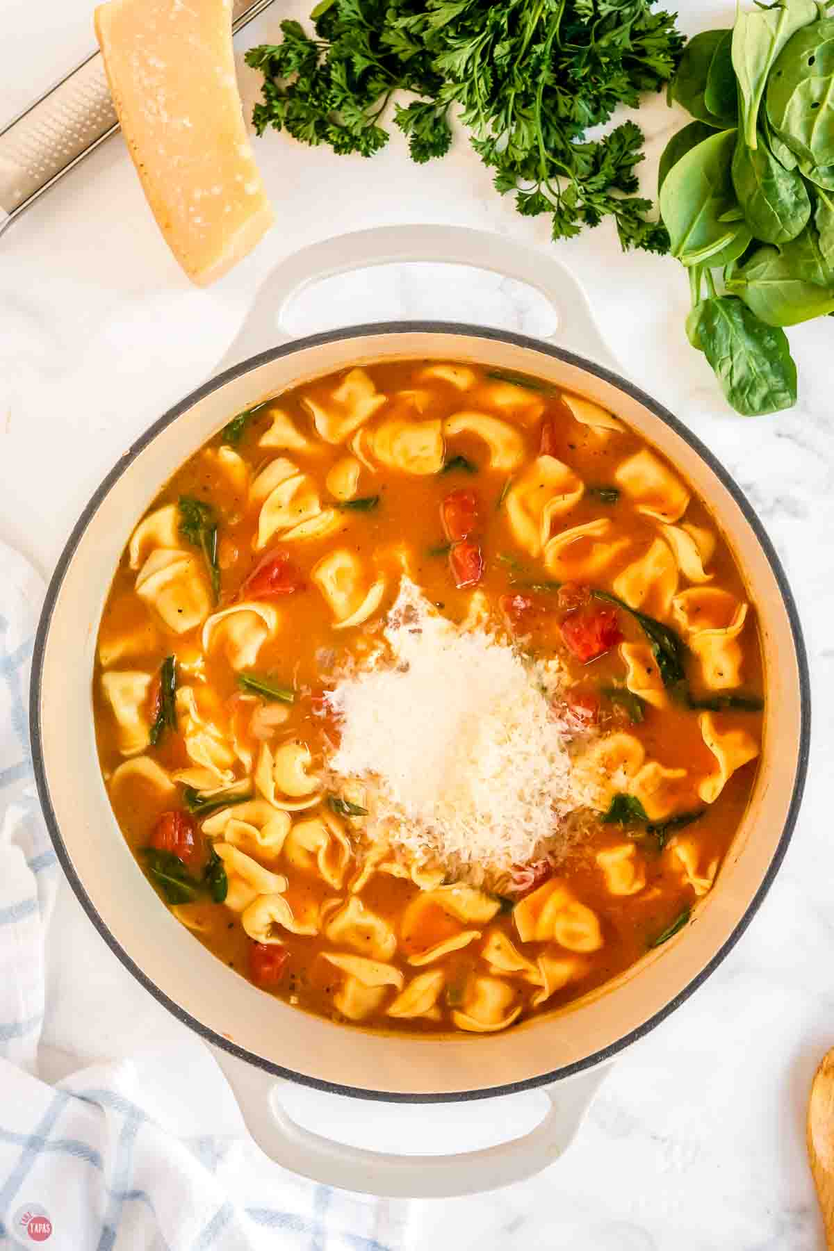 tortellini soup in a white pot with a small pile of grated cheese on top