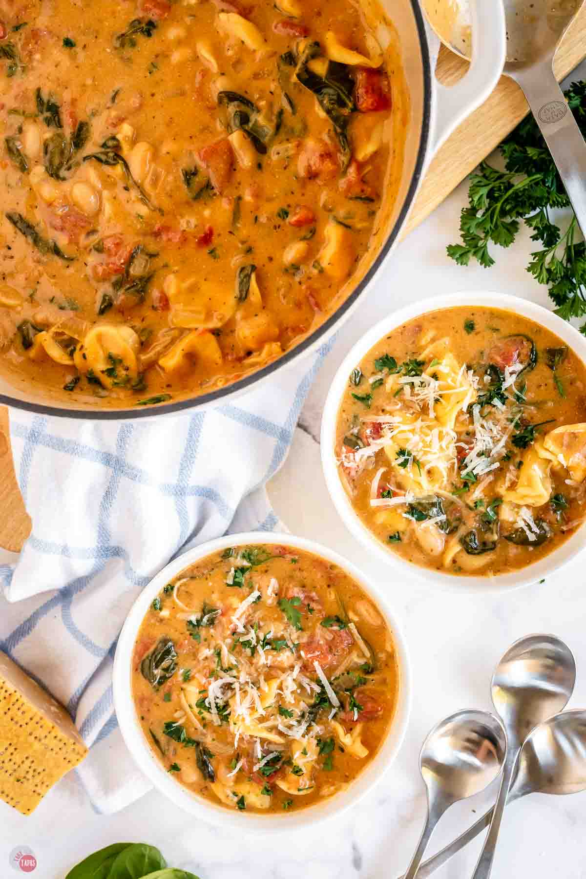 two bowls of soup next to a large white pot and two spoons