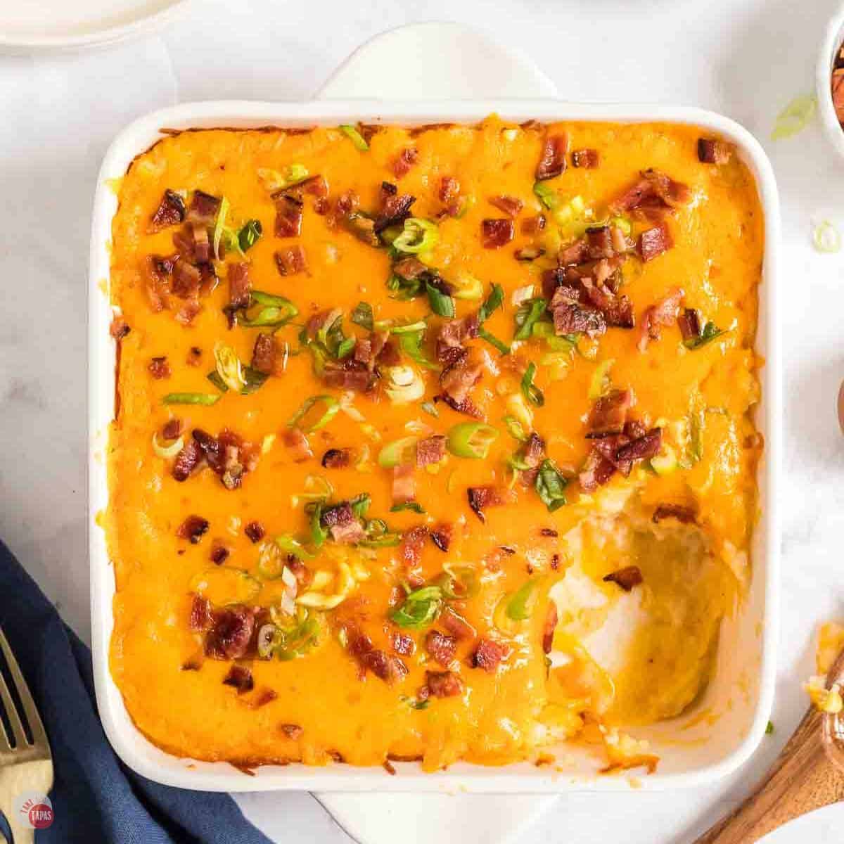 white baking dish with cheesy potato casserole and a scoop missing