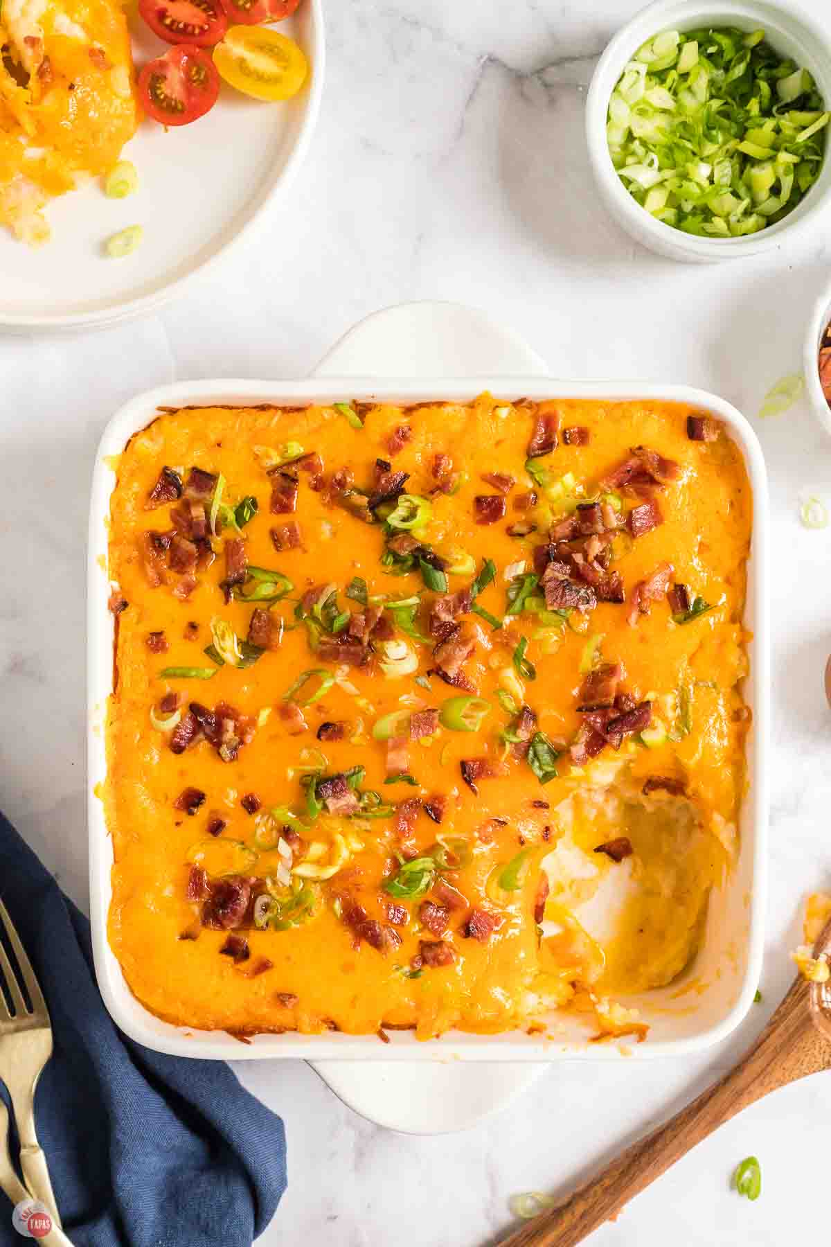 white baking dish with cheesy potato casserole and a scoop missing