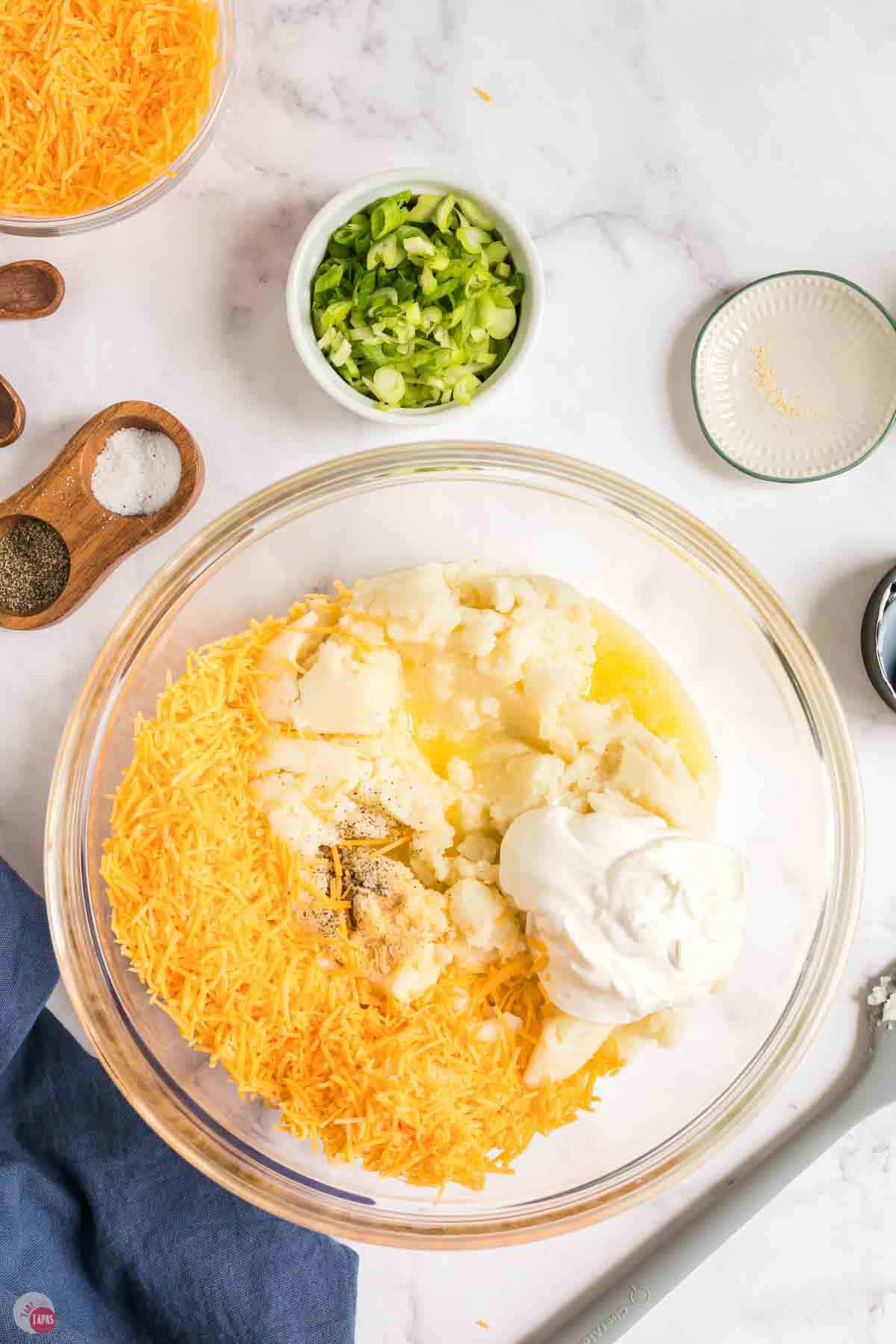 clear mixing bowl of mashed potatoes, cheese, sour cream, and melted butter