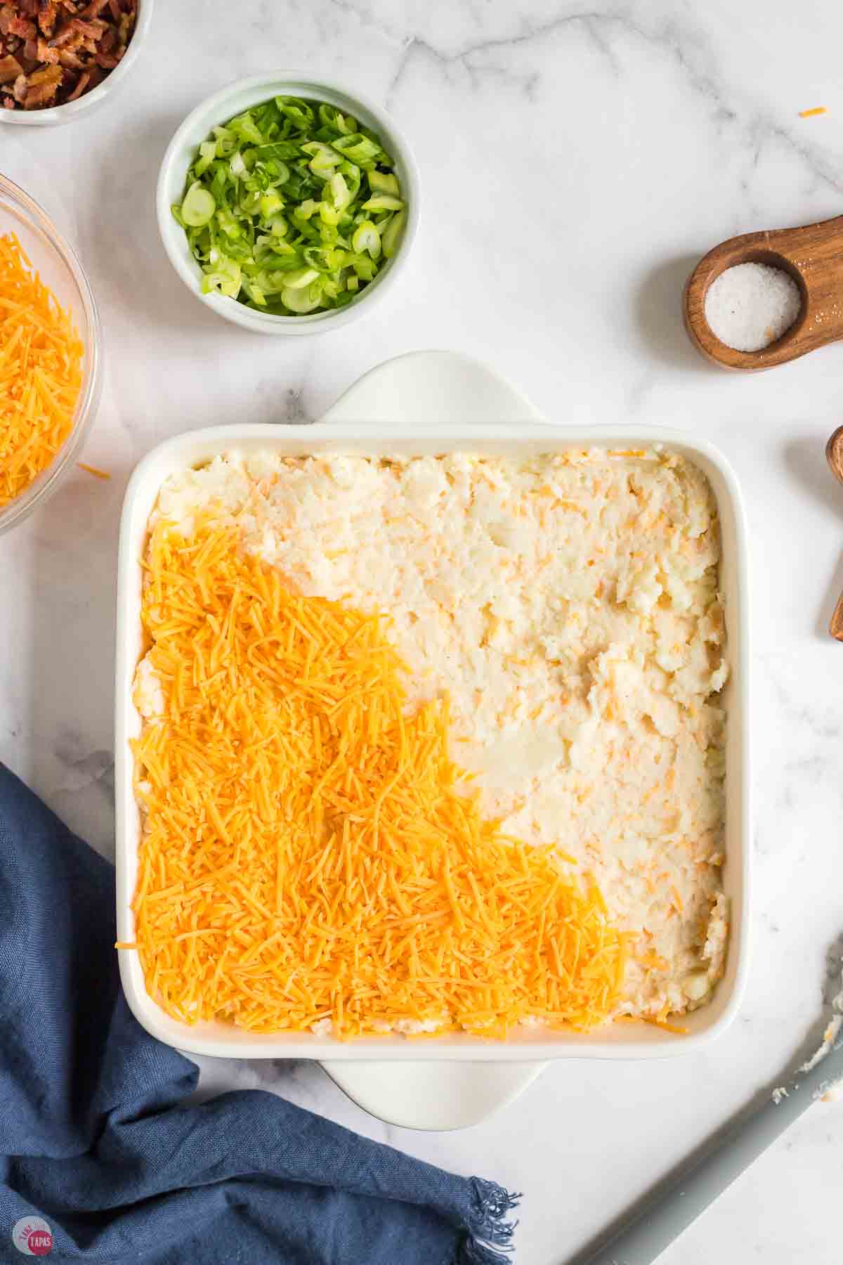 square baking dish full of potato mixture and half topped with shredded cheese