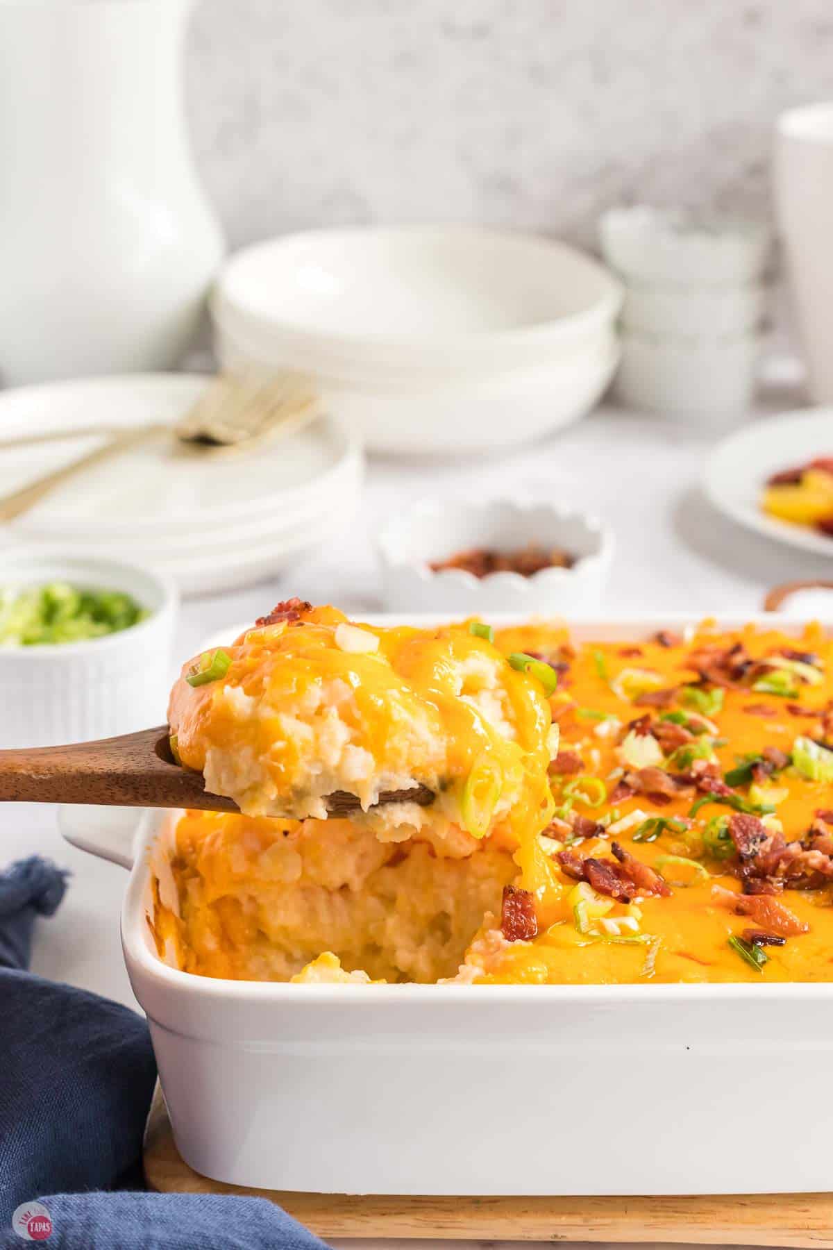wood spoon scooping potato casserole out of a white dish