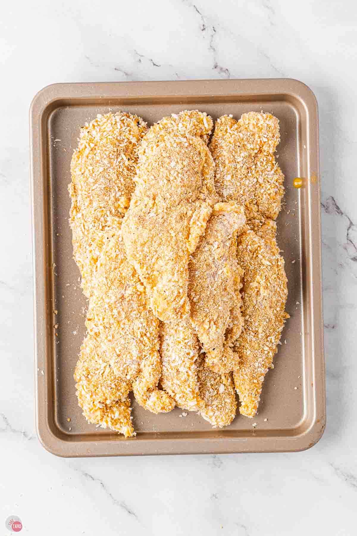dredged and coated chicken tenders on a baking sheet