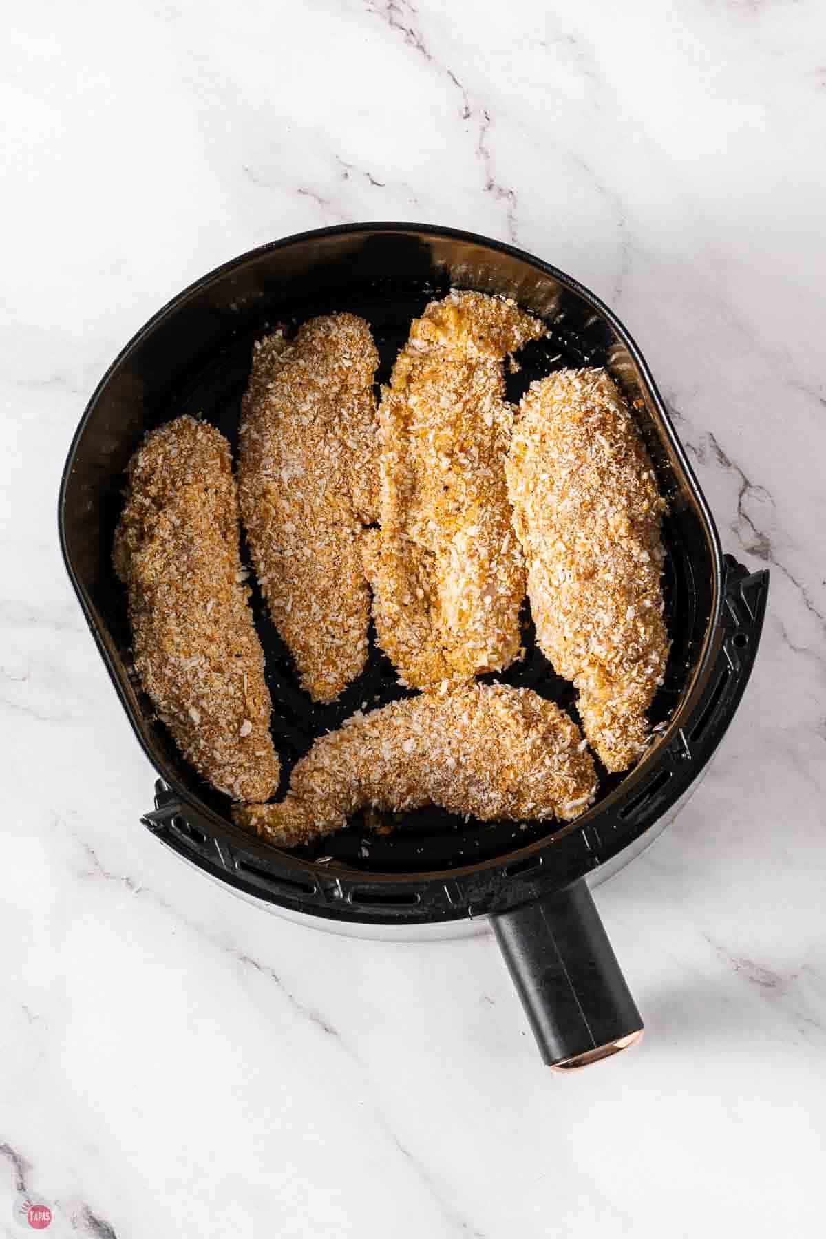 coated chicken tenders in a black air fryer basket