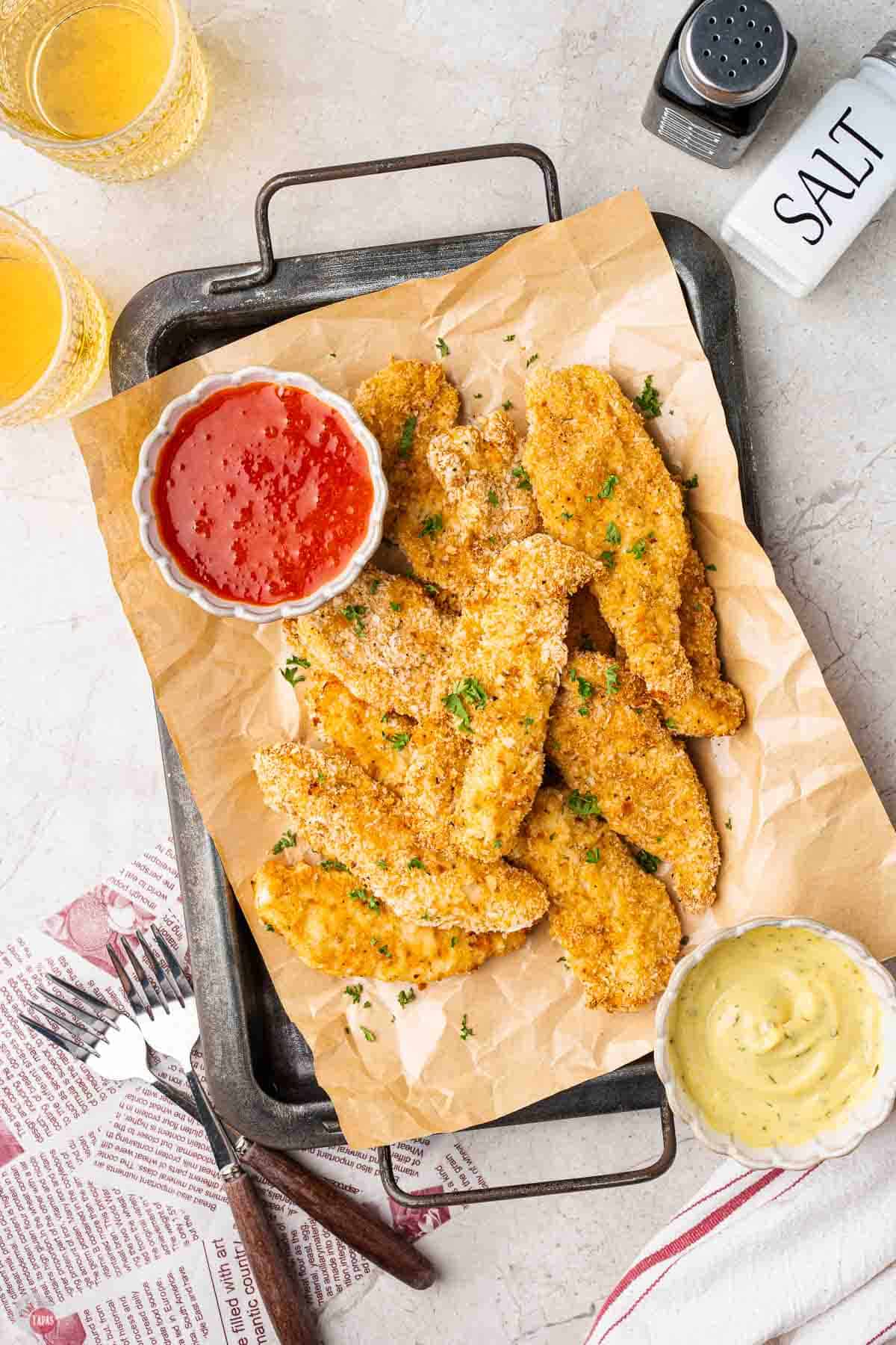 baking sheet with parchment paper and chicken tenders along with two types of sauce