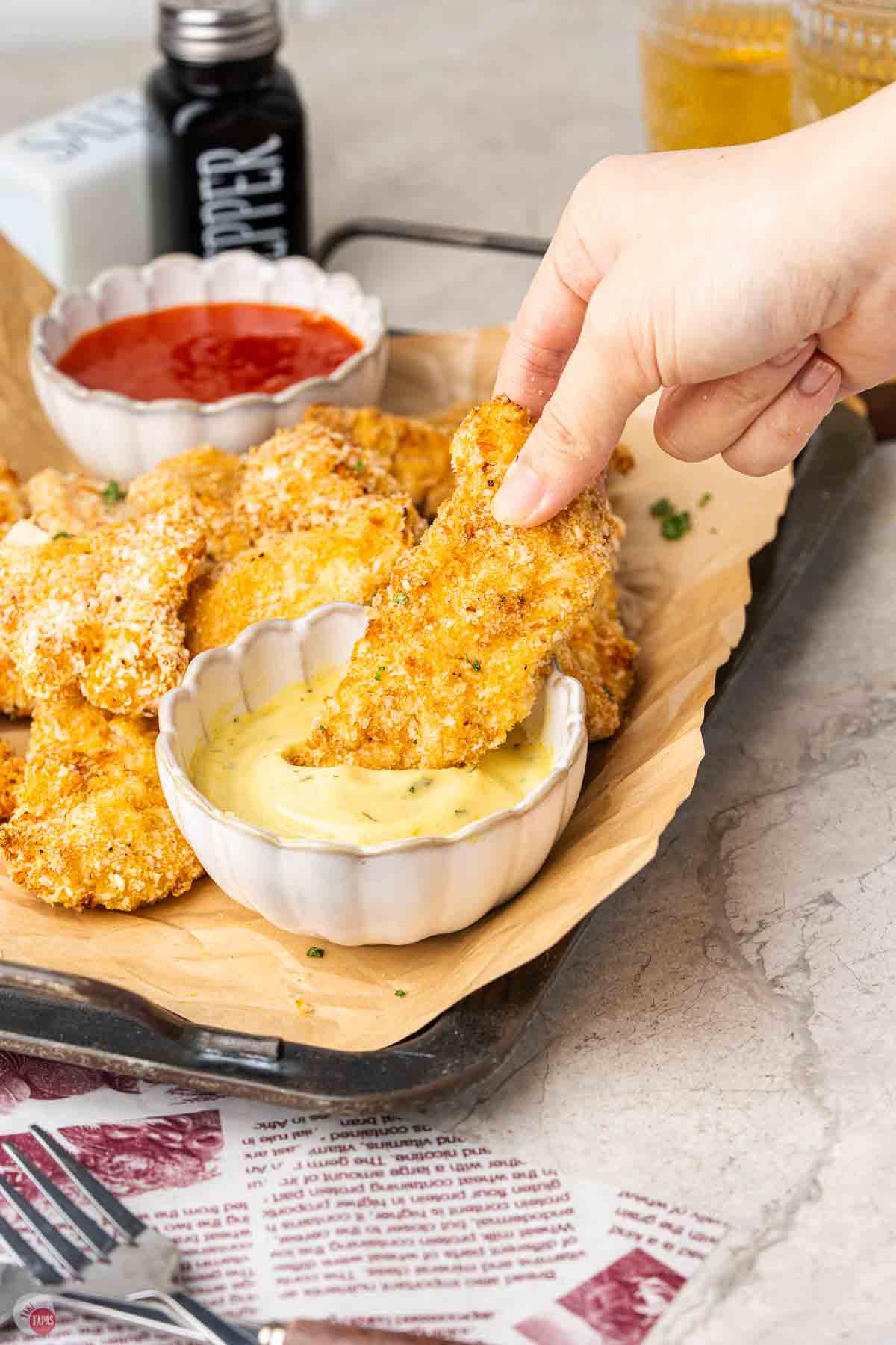 hand dipping a chicken tender in a bowl of sauce
