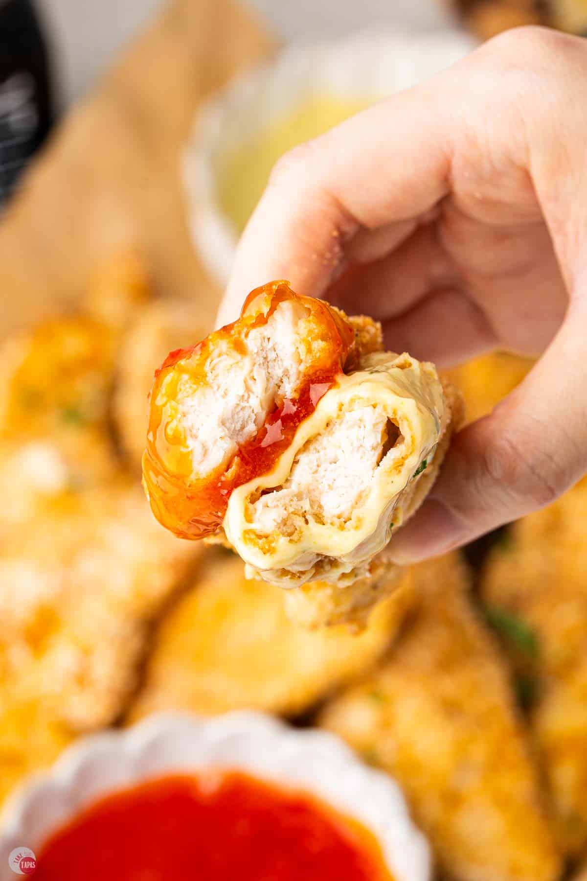 hand holding chicken tender dipped in sauce and a bite taken out of it