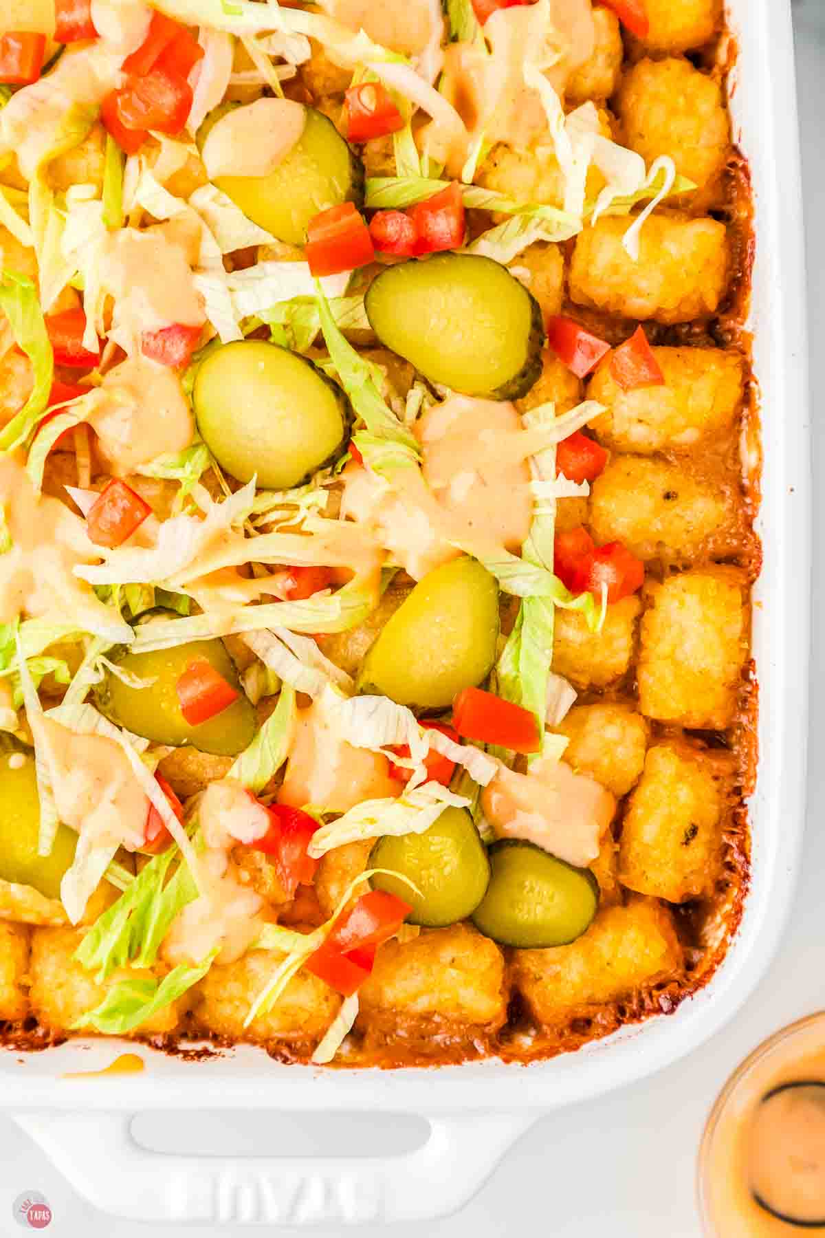 close up of big mac casserole topped with lettuce tomatoes and pickles
