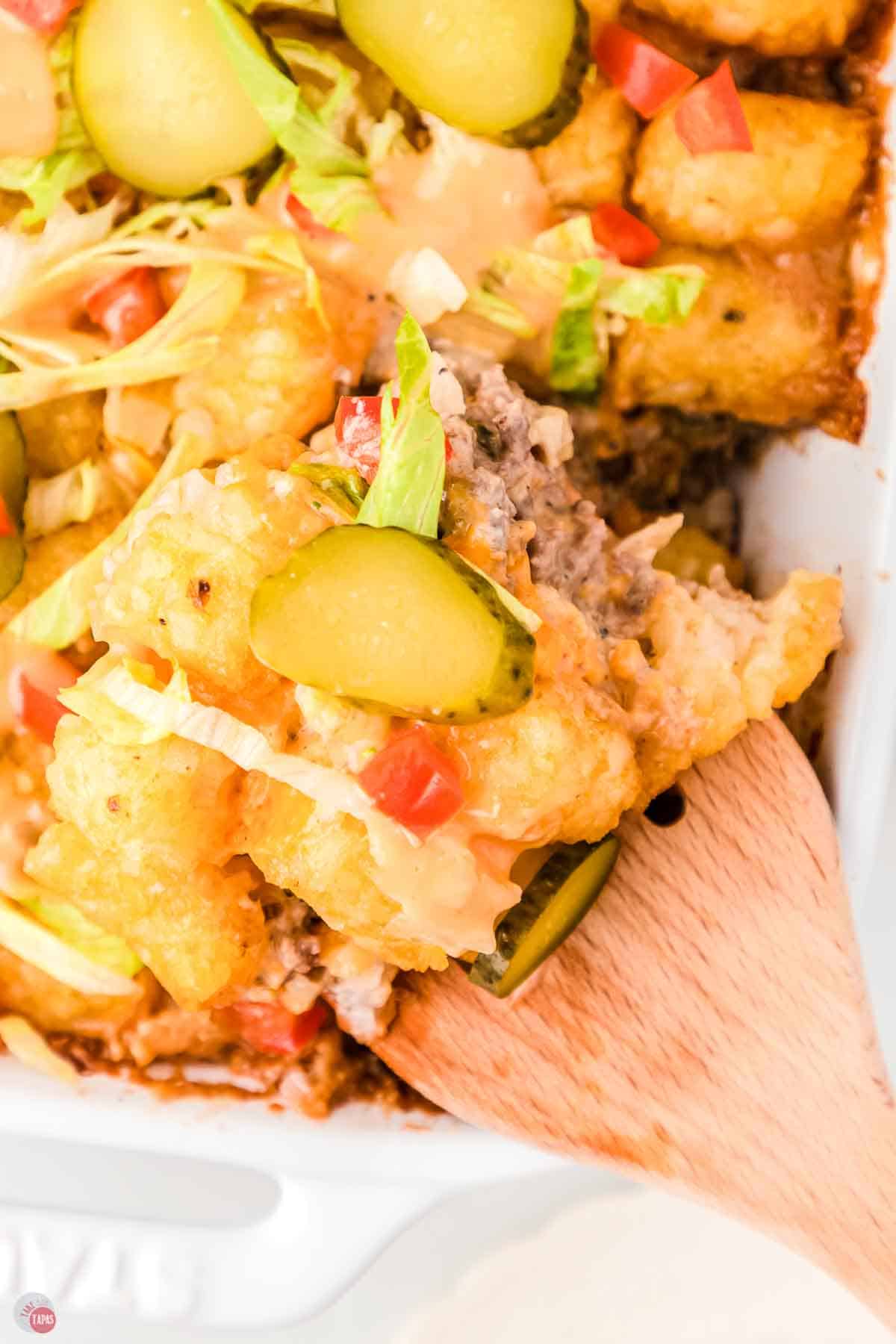 close up of a wood spatula with scoop of casserole with tater tots and pickles