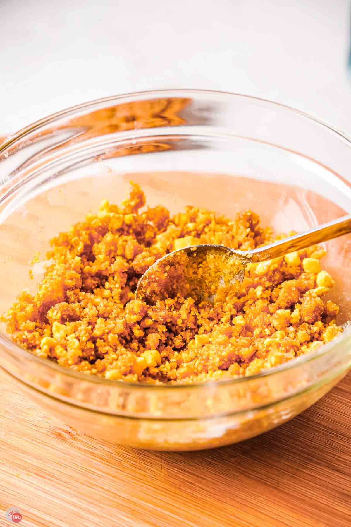 clear bowl of crushed cereal and melted butter being mixed with a spoon