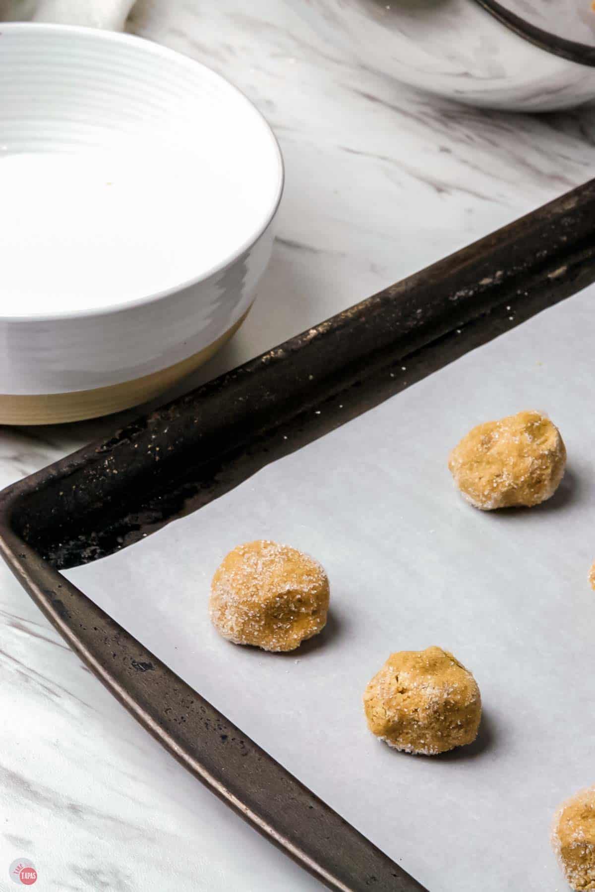 balls of cookie dough rolled in sugar on a parchment lined baking sheet