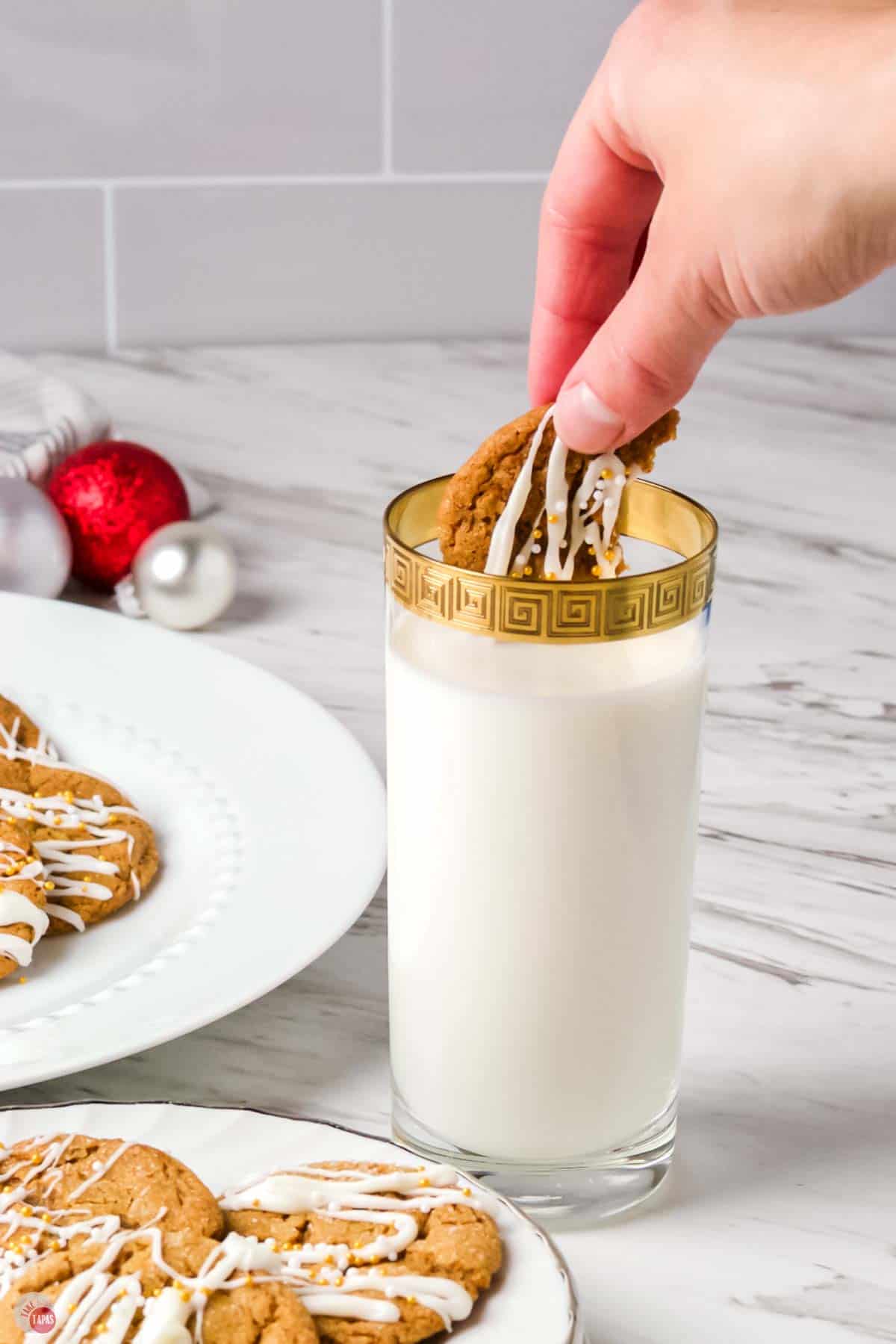 hand dunking a cookie in a glass of milk