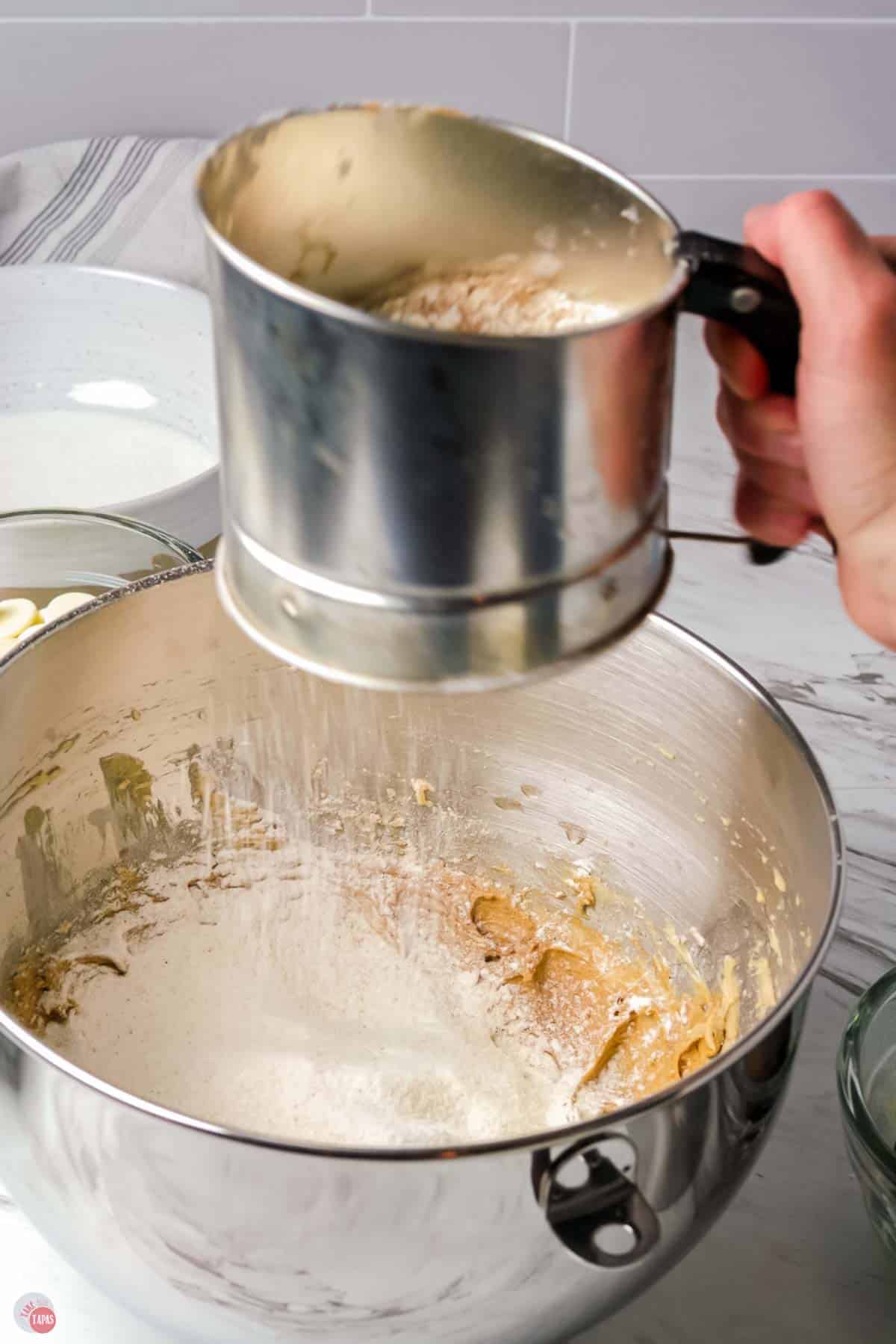 sifter sprinkling flour into a bowl of creamed butter and sugar
