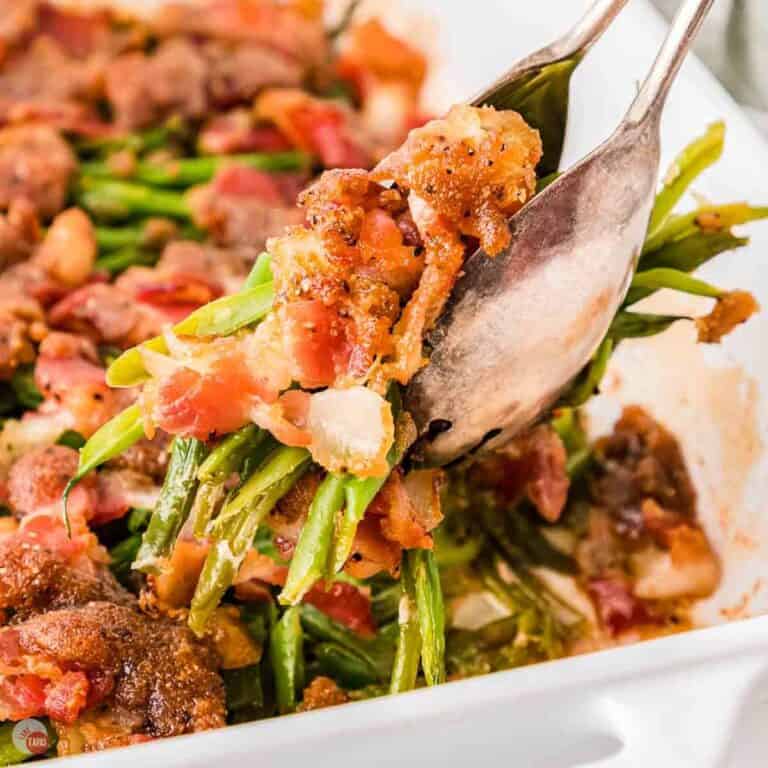 silver tongs with a bunch of green beans topped with bacon