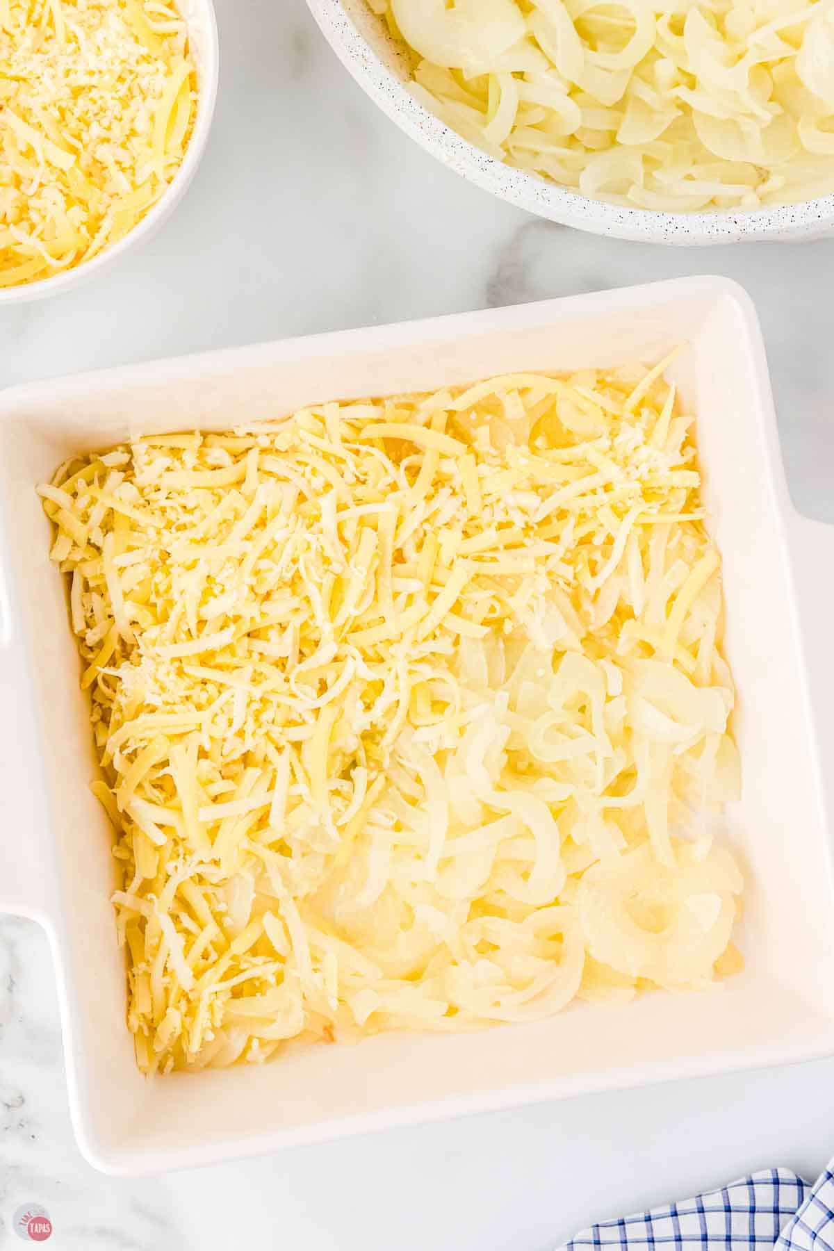 square baking dish with cooked onions and half topped with shredded cheese