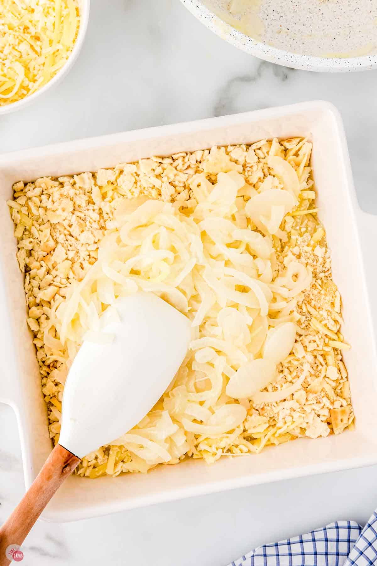 white baking dish with crushed crackers and topped with sliced onions