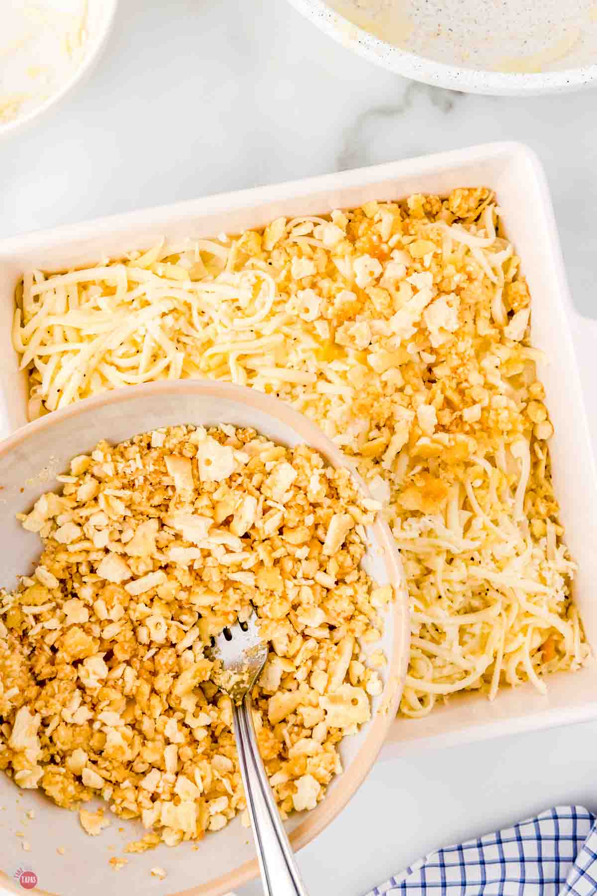 square white baking dish filled with onions and cheese and being topped with buttered crushed crackers