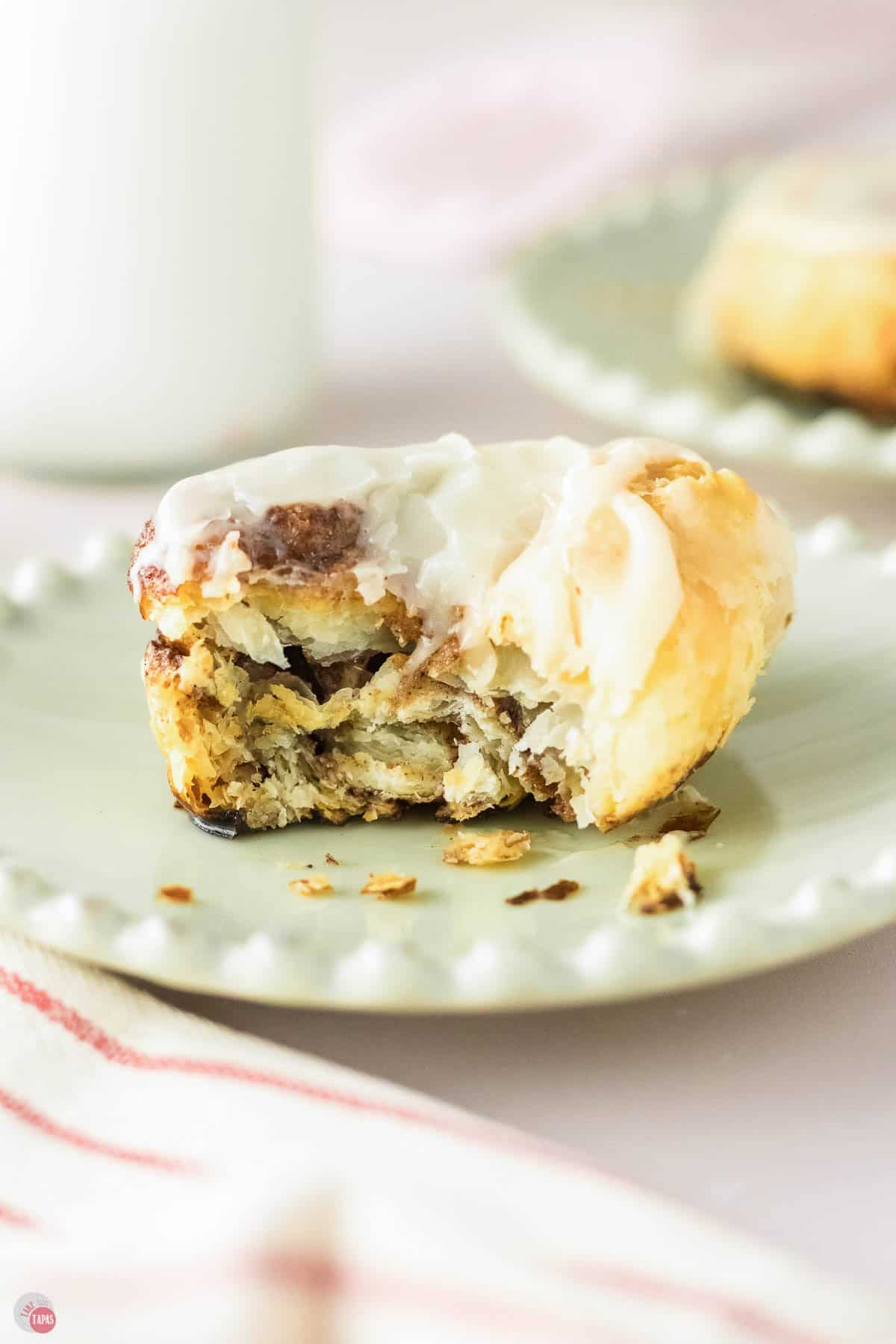 green plate with cinnamon roll on top and a bite missing out of it