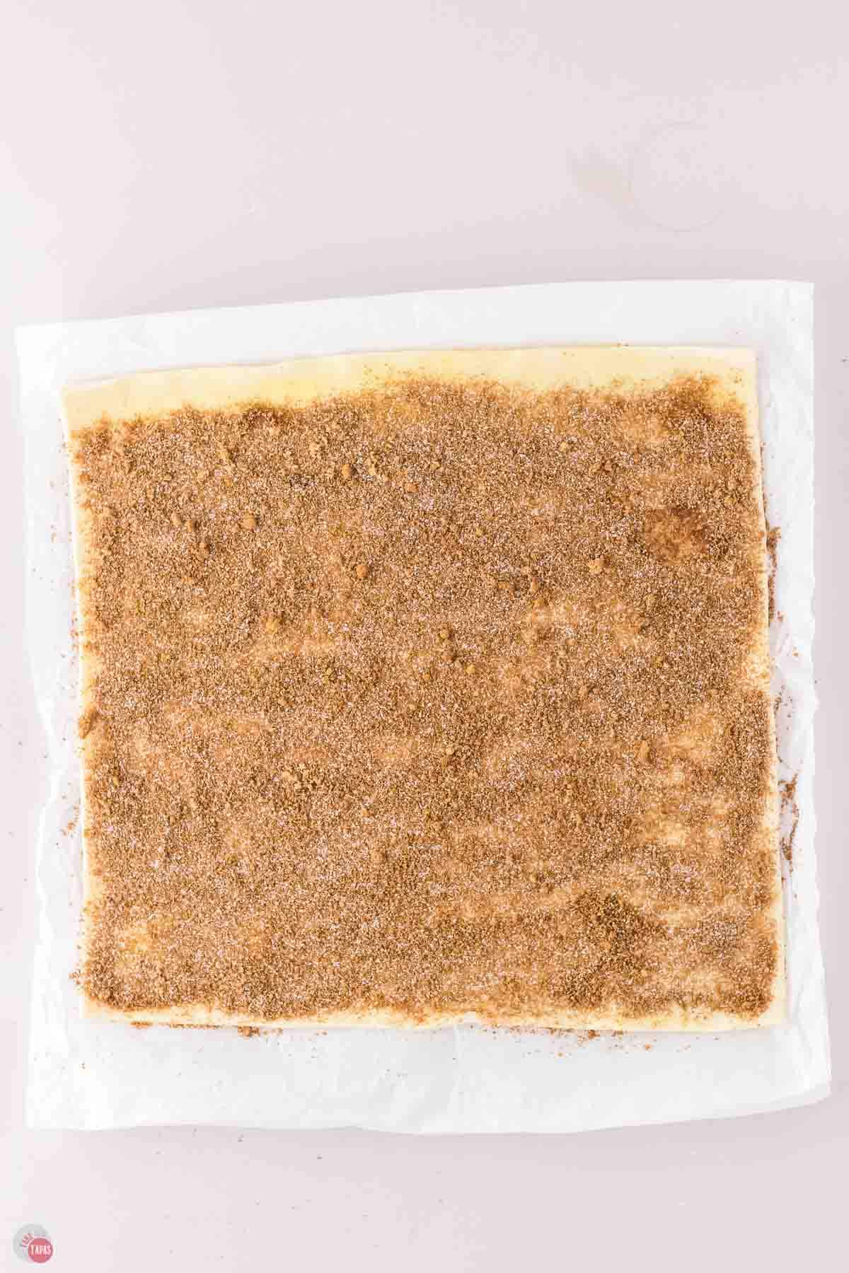 sheet of puff pastry on parchment paper and topped with butter, cinnamon, and sugar