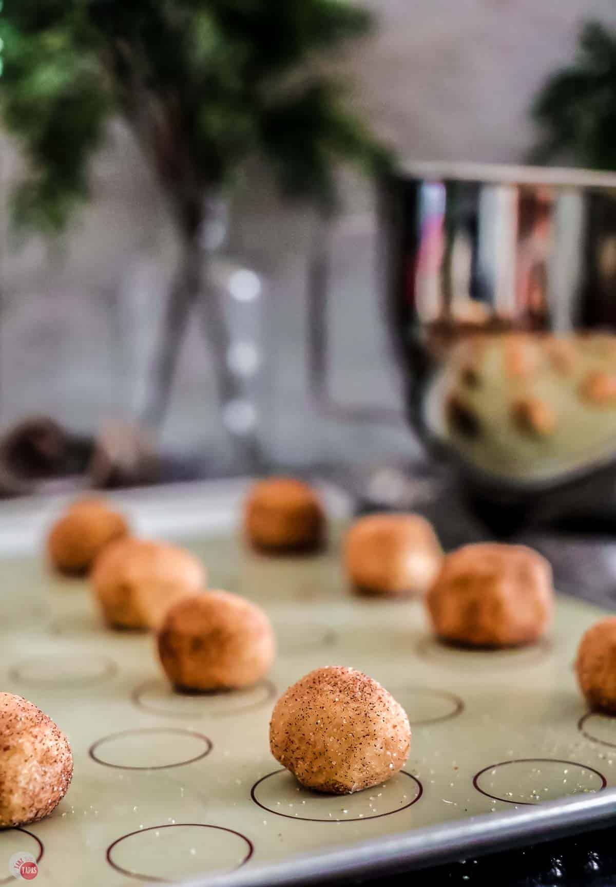 balls of cookie dough coated in cinnamon and sugar on a baking sheet
