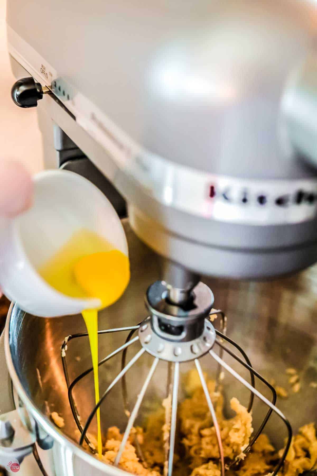 egg being dropped into a mixer bowl