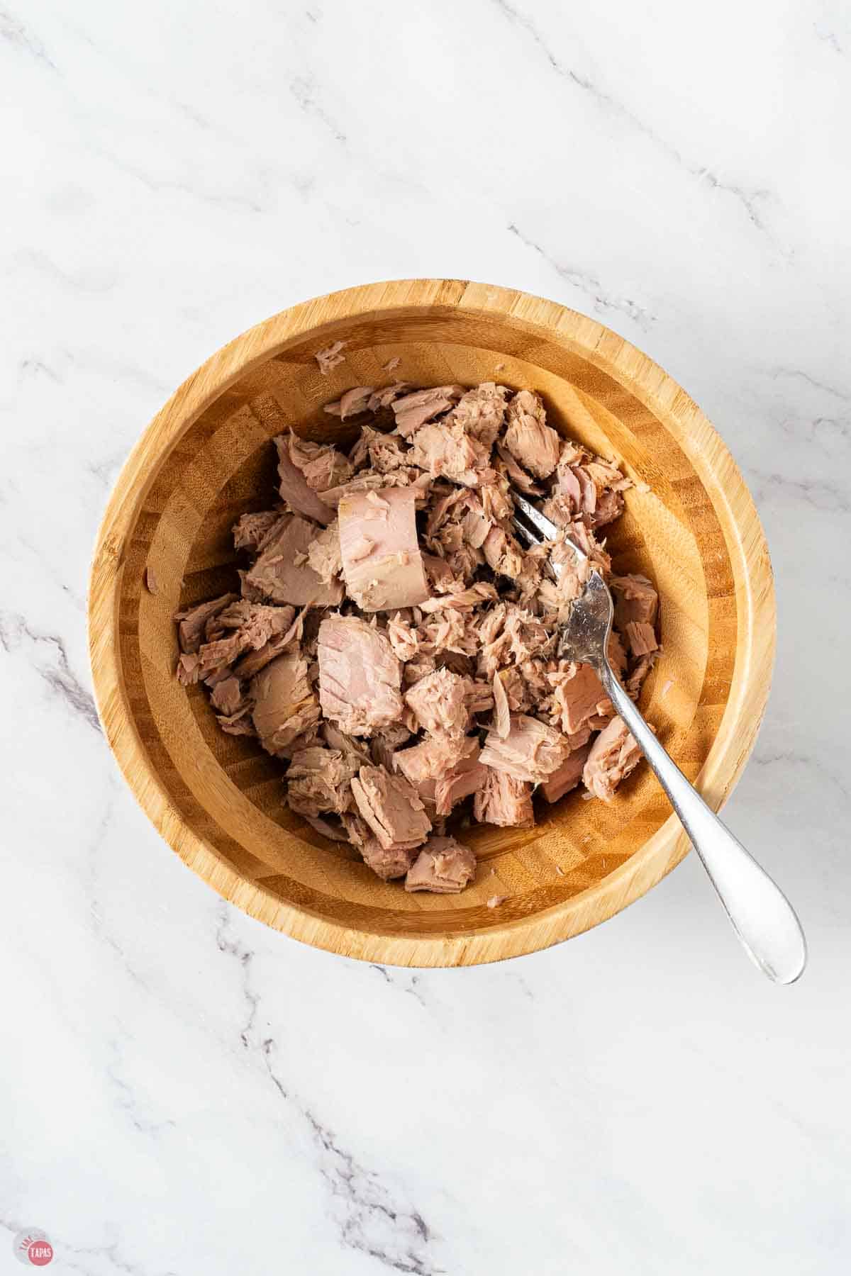 flaky tuna in a brown wood bowl with a fork stirring it up