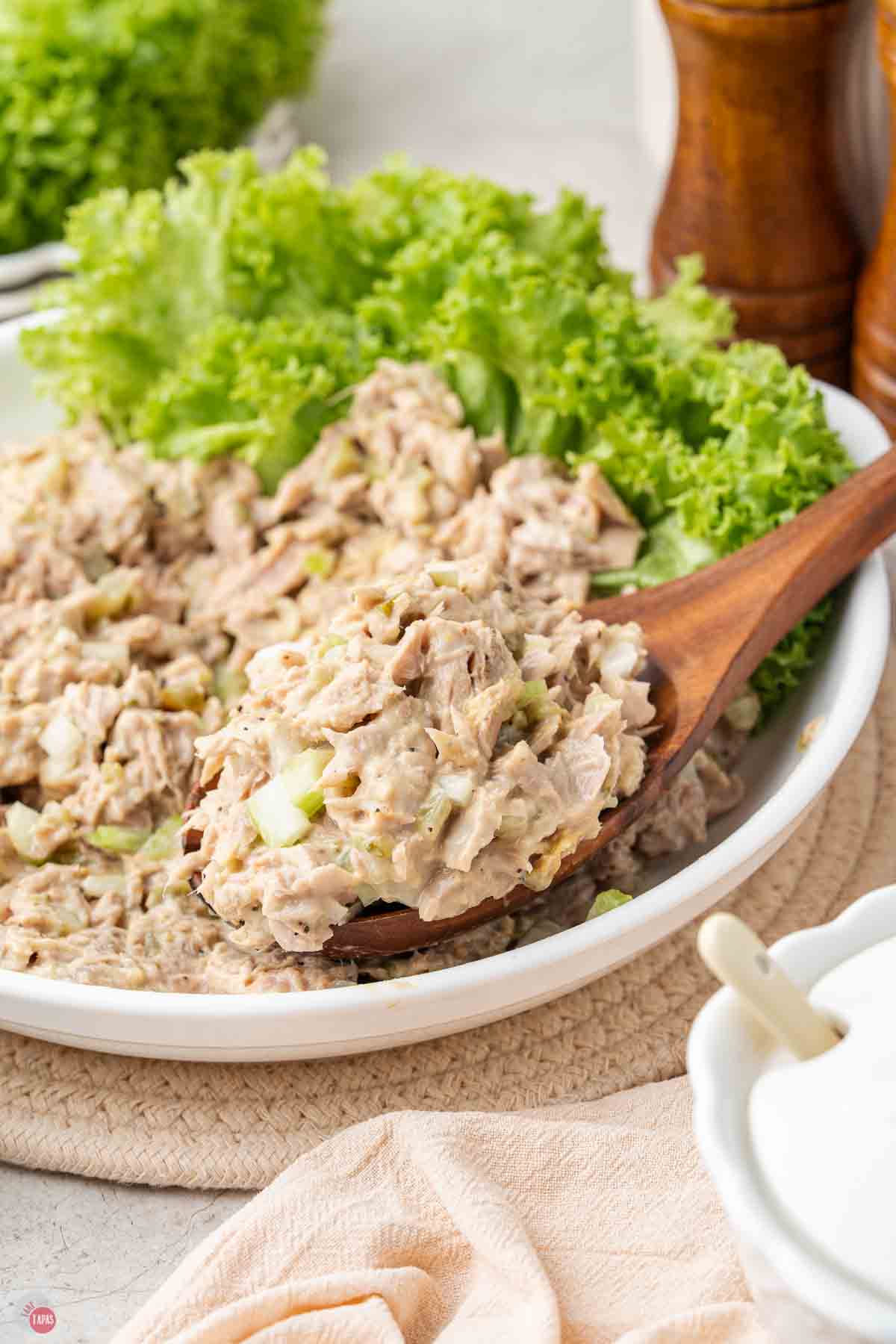 bowl of tuna salad with green leaf lettuce under it and a wood spoon