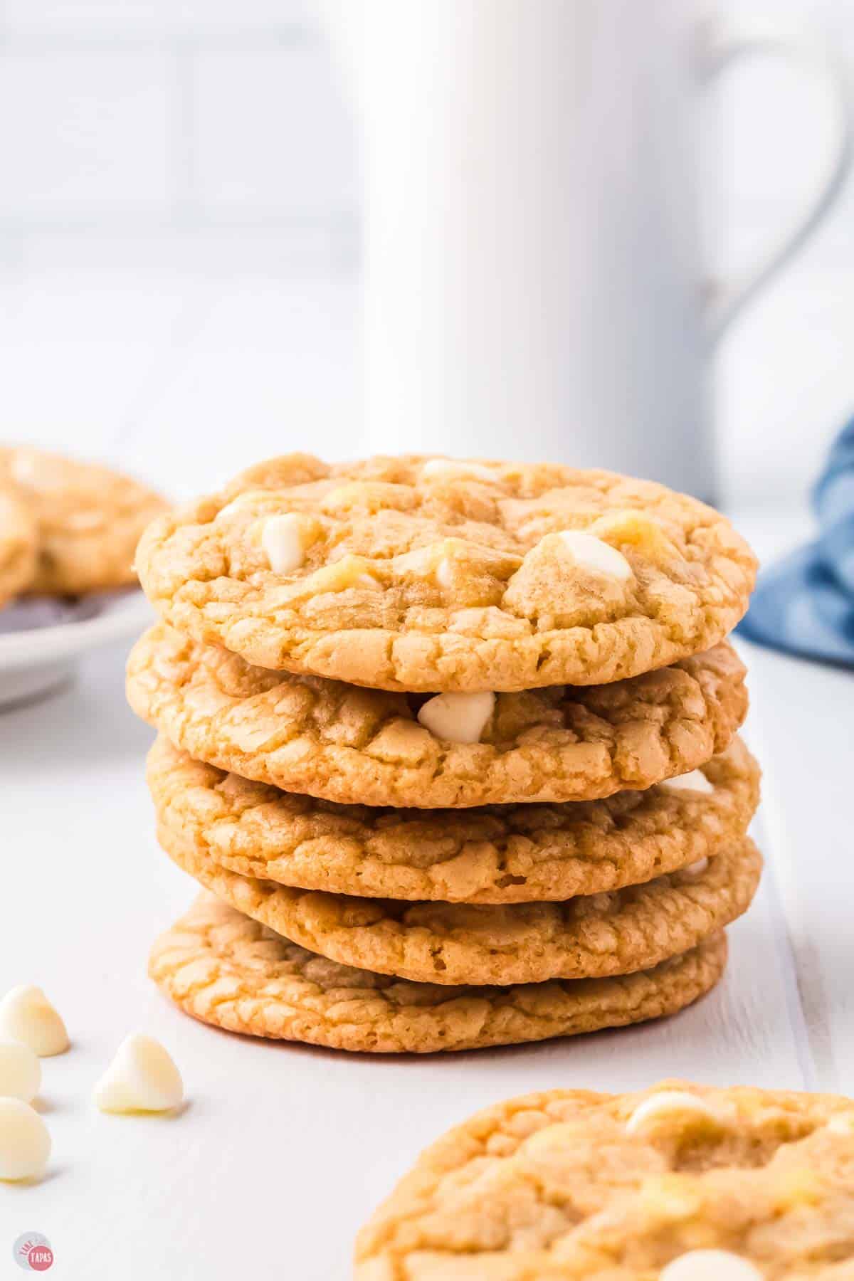 stack of white chocolate chip cookies on a table with a glass of milk