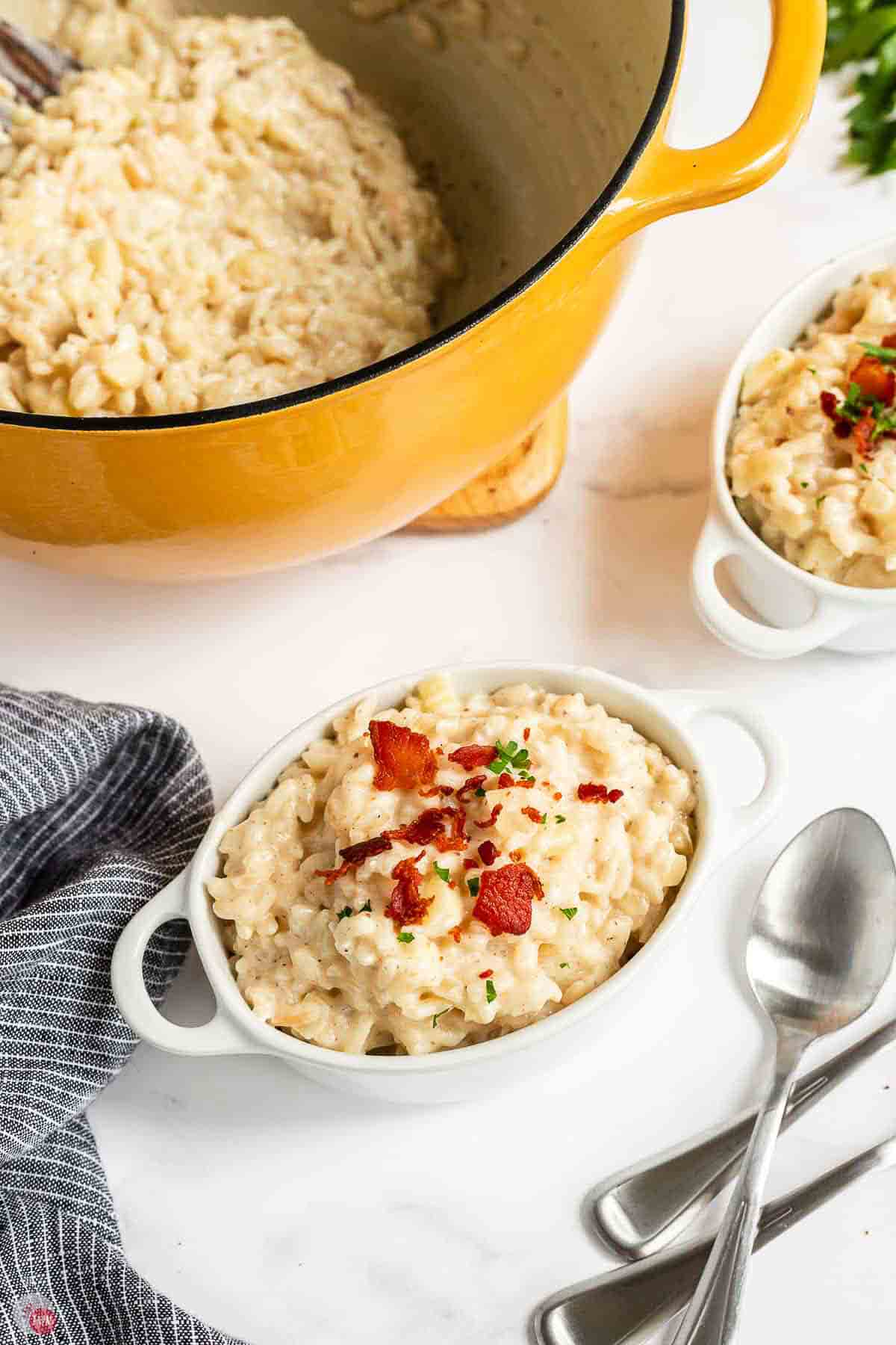 Bowl of apple risotto with bacon next to a pot and a spoon
