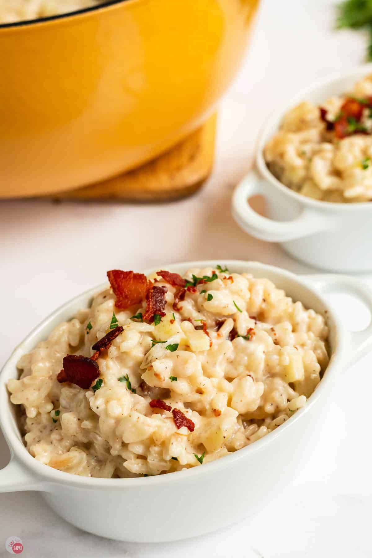 Apple risotto with crumbled bacon in a white bowl next to the pot