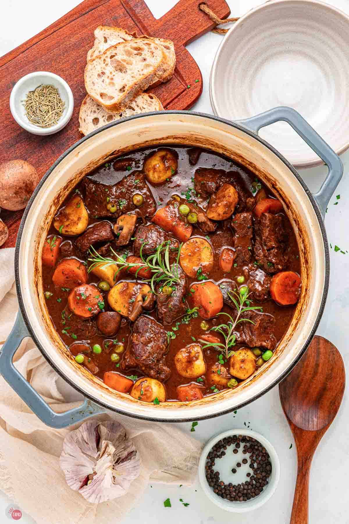 pot of red wine beef stew next to a bowl and a spoon