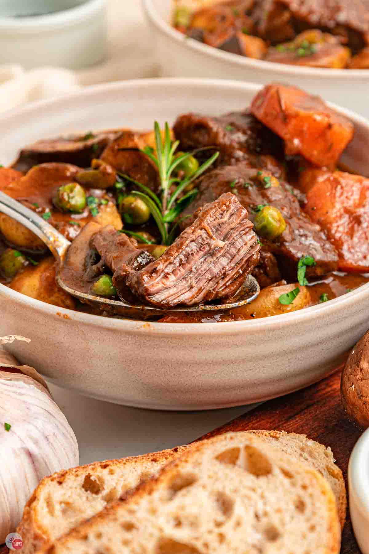 bowl of beef stew next to bread slices