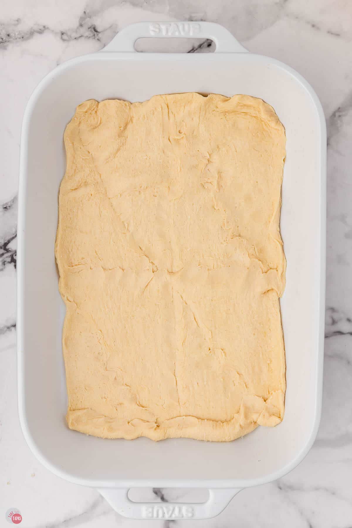 crescent roll dough pressed into the bottom of a white baking dish