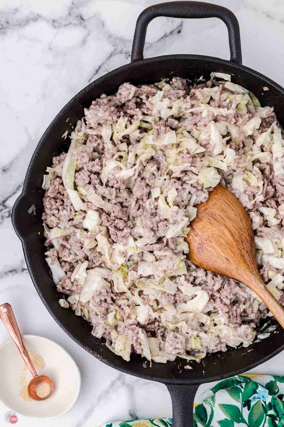 ground beef and cabbage mixture being stirred in a skillet with wood spoon