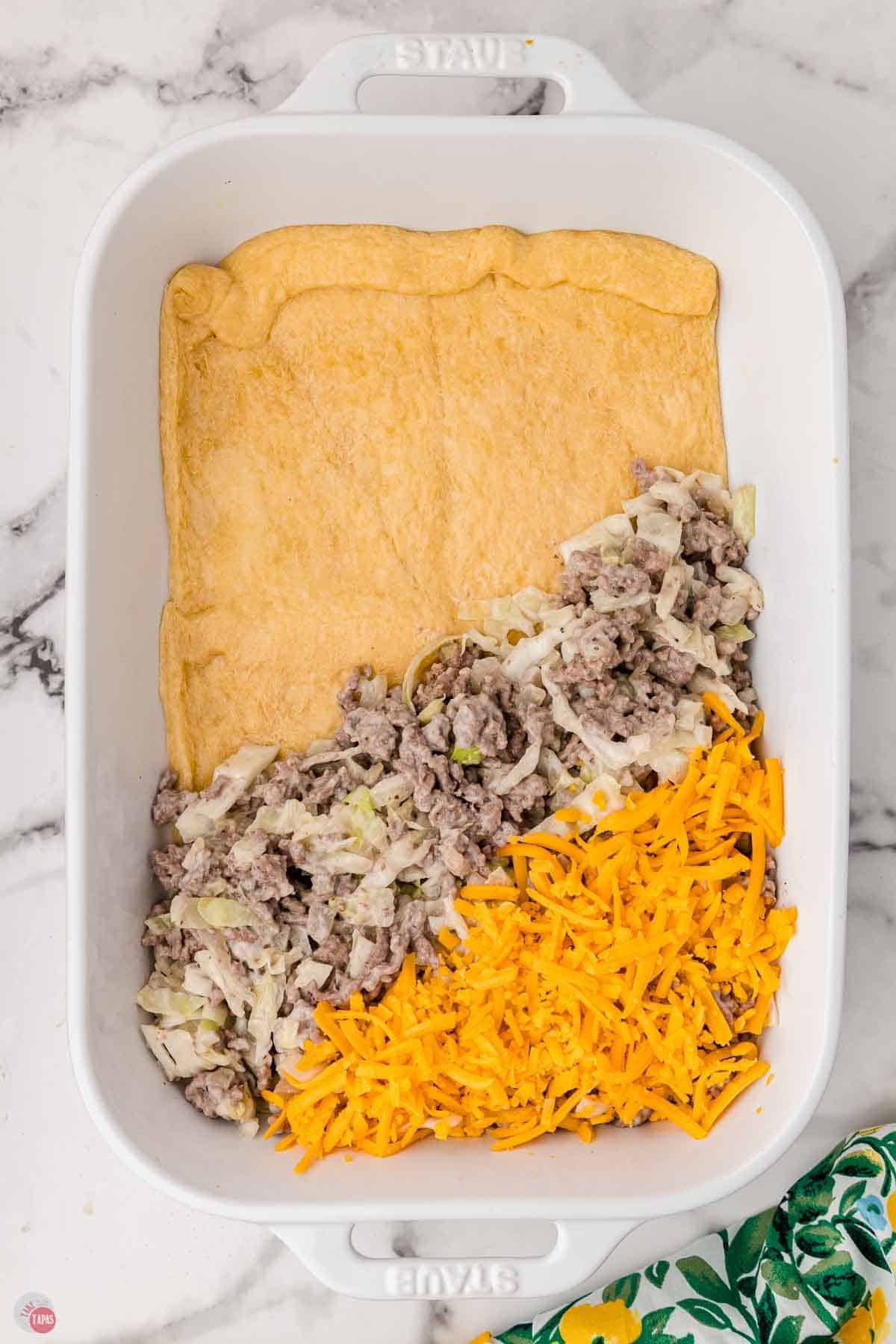 casserole being layered with crust, ground beef, and shredded cheese