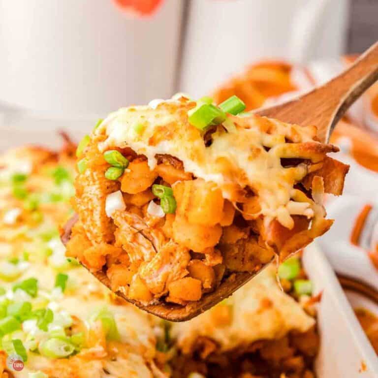 wood spoon with a scoop of buffalo chicken potato casserole topped with cheese and green onions