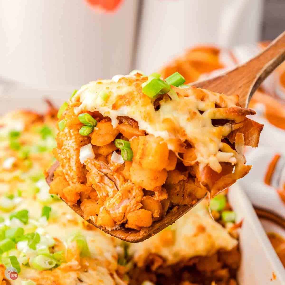 wood spoon with a scoop of buffalo chicken potato casserole topped with cheese and green onions