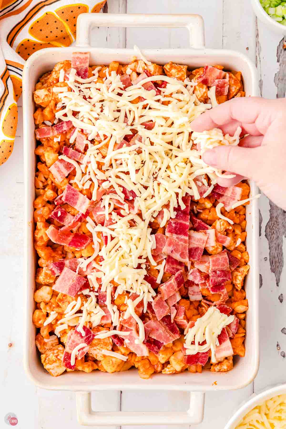 buffalo chicken casserole with bacon and shredded cheese being sprinkled on top