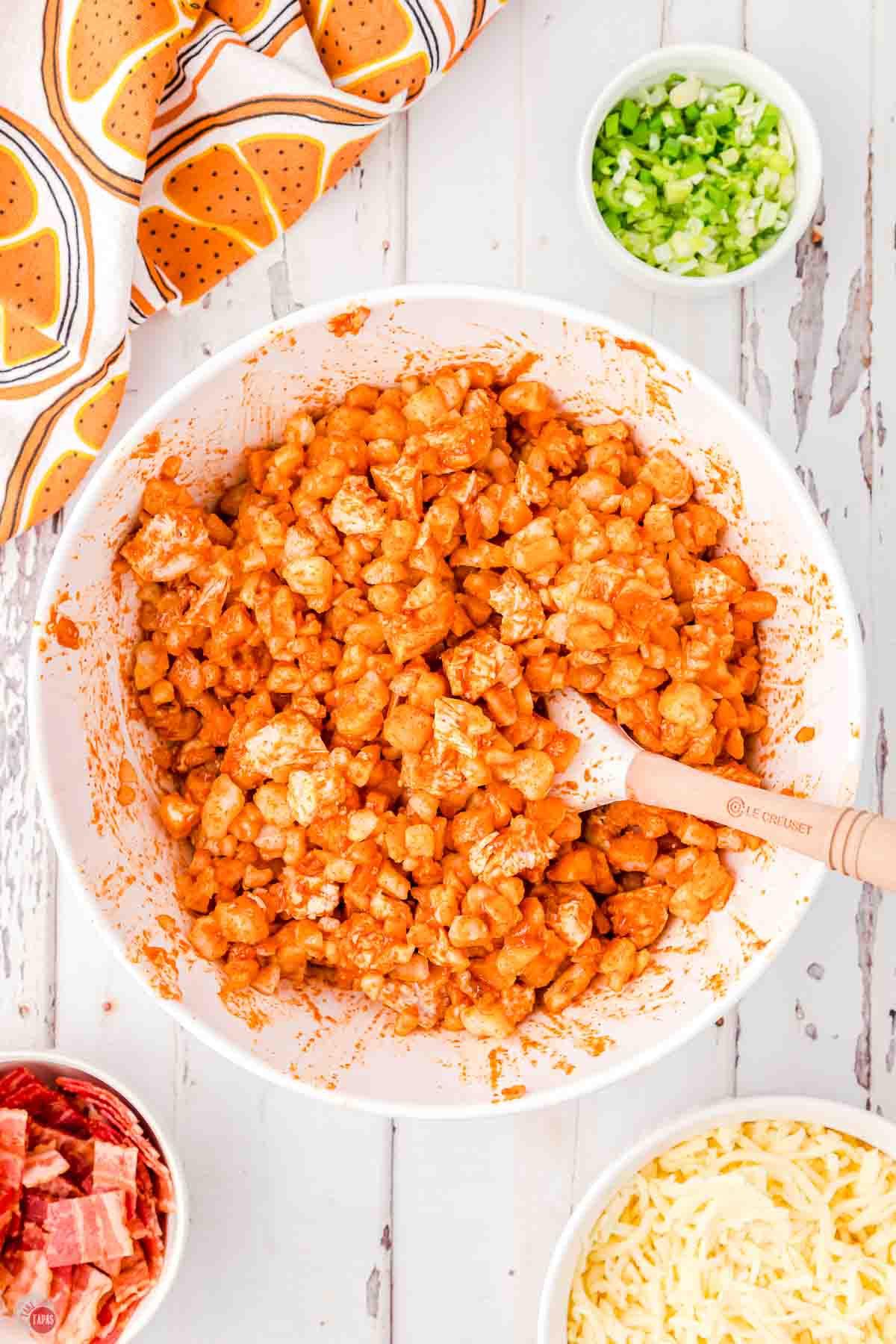 chicken and potatoes being tossed with buffalo sauce in a large white bowl