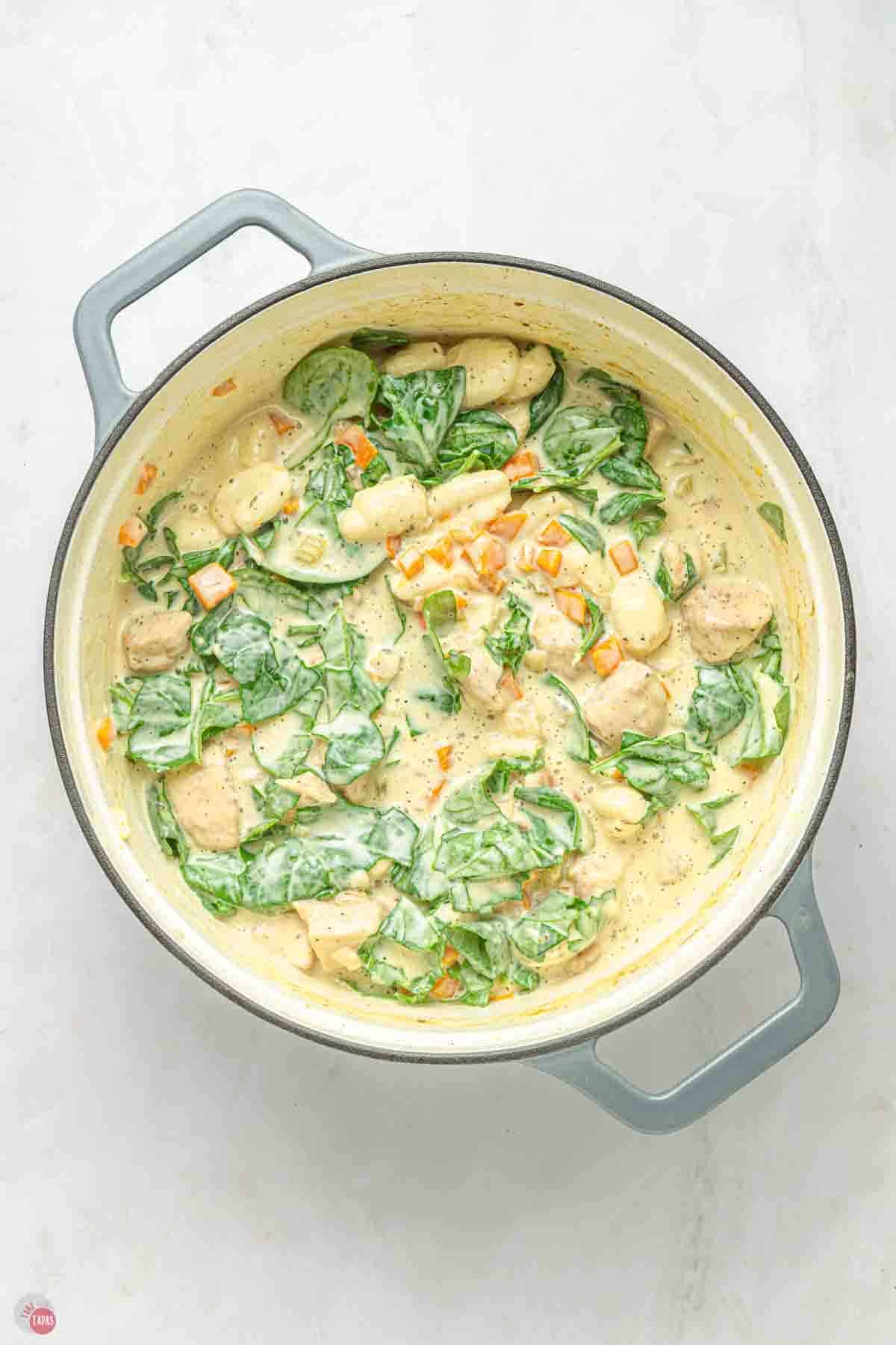 pot of chicken and gnocchi soup with spinach stirred in