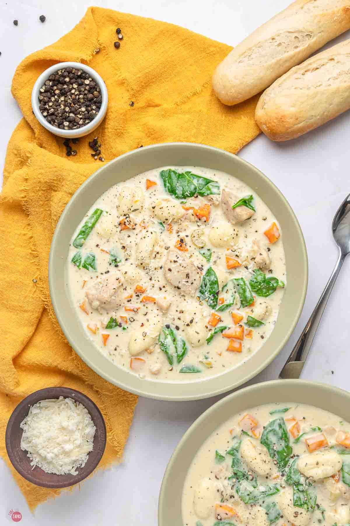 two bowls of chicken gnocchi soup next to bread loaves