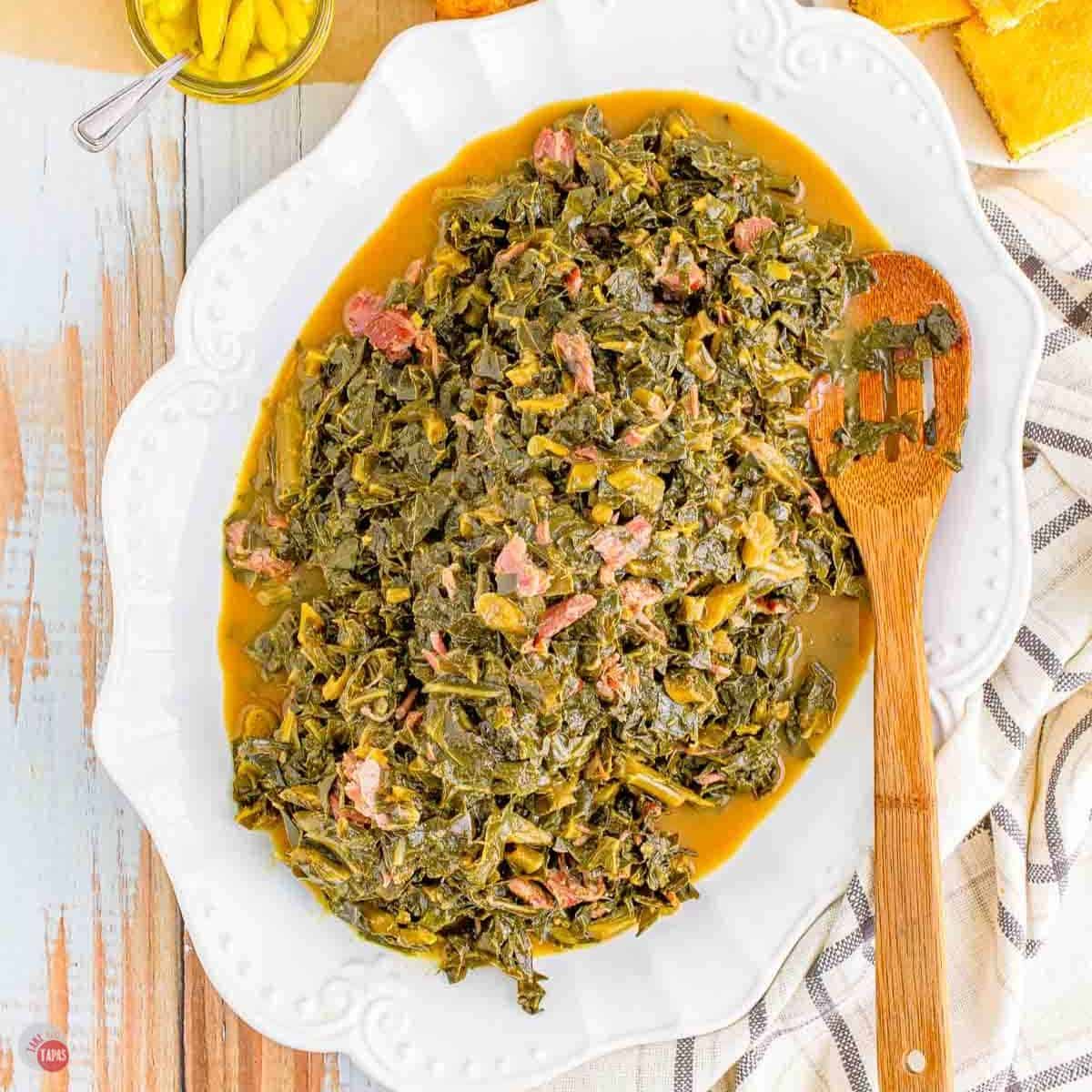 white platter of collard greens with ham hocks and a wood spoon