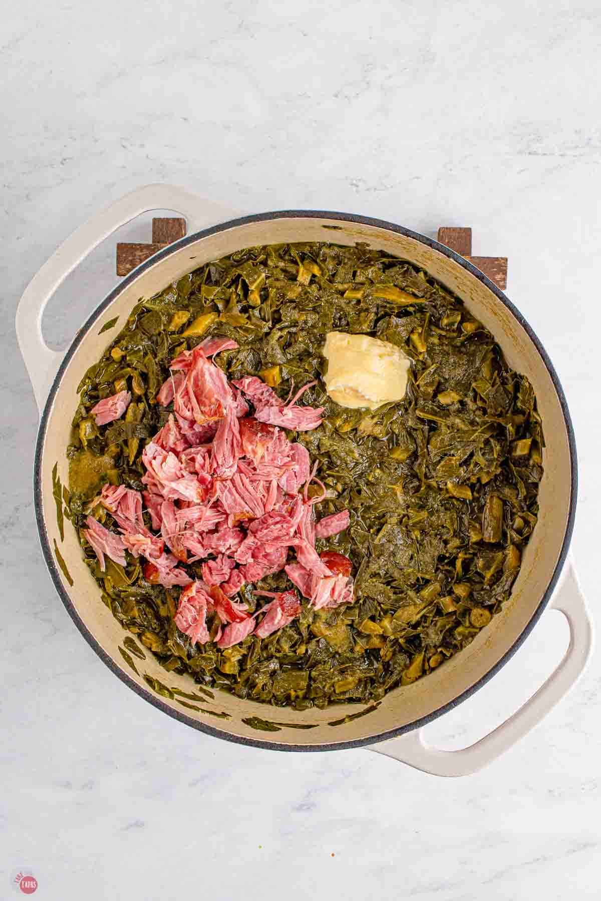 cooked collard greens in a dutch oven with shredded ham and butter